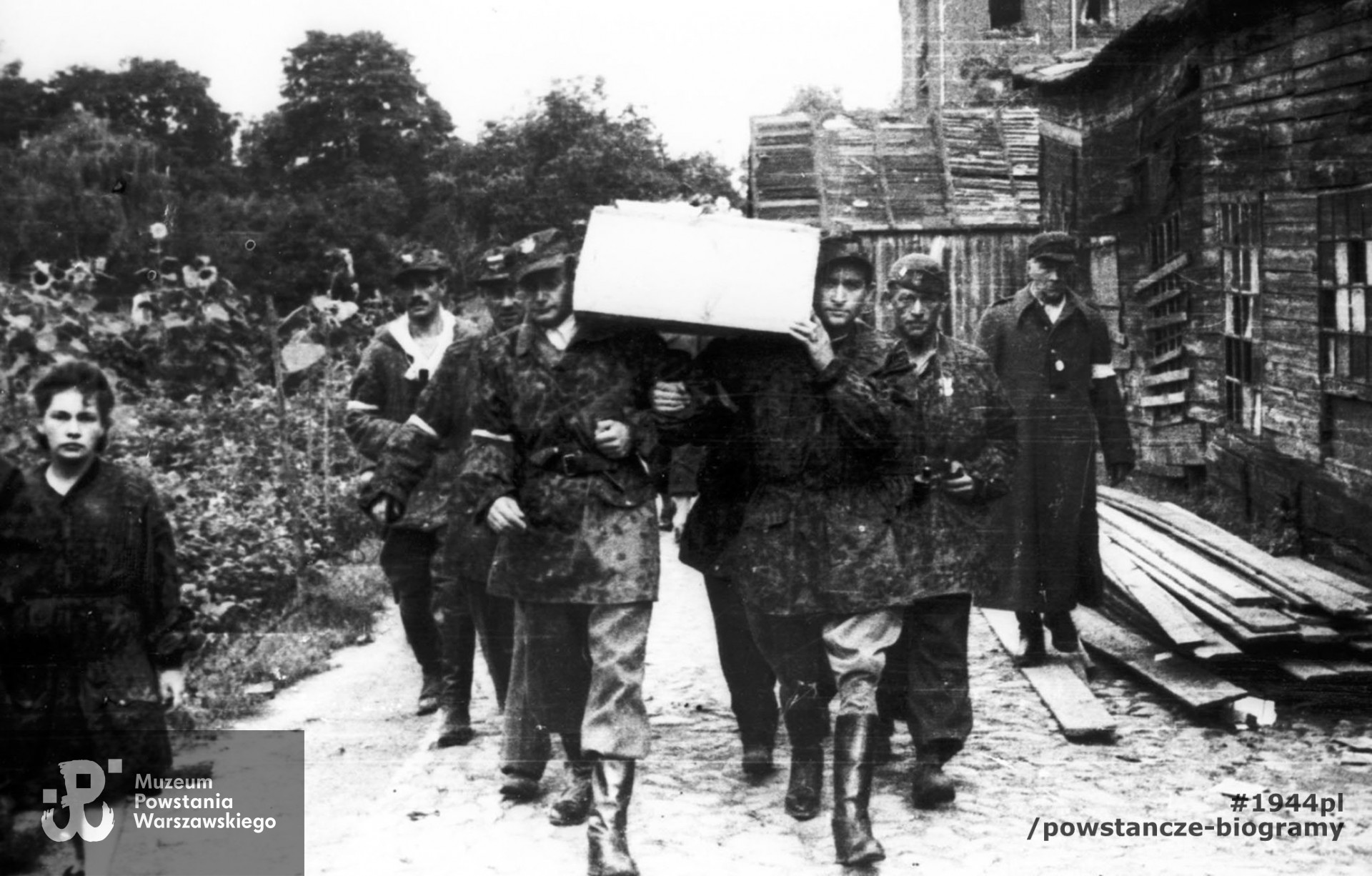 Fotografia z Powstania Warszawskiego. Wola. Żołnierze kompanii "Zemsta" batalionu "Pięść" niosący trumnę poległego ppor. Tadeusza Towarnickiego "Naprawa". Trumnę niosą ppor. Kazimierz Barszczewicz "Henryk" i ppor. NN "Ryś". Z lewej widoczny ppor. Jan Kowalczyk "Kieł", z lornetką po prawej Eugeniusz Kuźwa "Hipek" dowódca 169 plutonu batalionu "Kiliński". W tle po prawej widoczny budynek Zakładu dla umysłowo niedorozwiniętych na posesji Karolkowa 77. Autorem zdjęcia jest Stefan Bałuk. Fot. ze zbiorów Muzeum Powstania Warszawskiego, sygn. MPW-IH/3444. Zdjęcie dostępne także w Fototece MPW, sygn. <a href=" http://www.1944.pl/galerie/fototeka/foto/7782/?szukaj=barszczewicz"> MPW-IS/149</a>