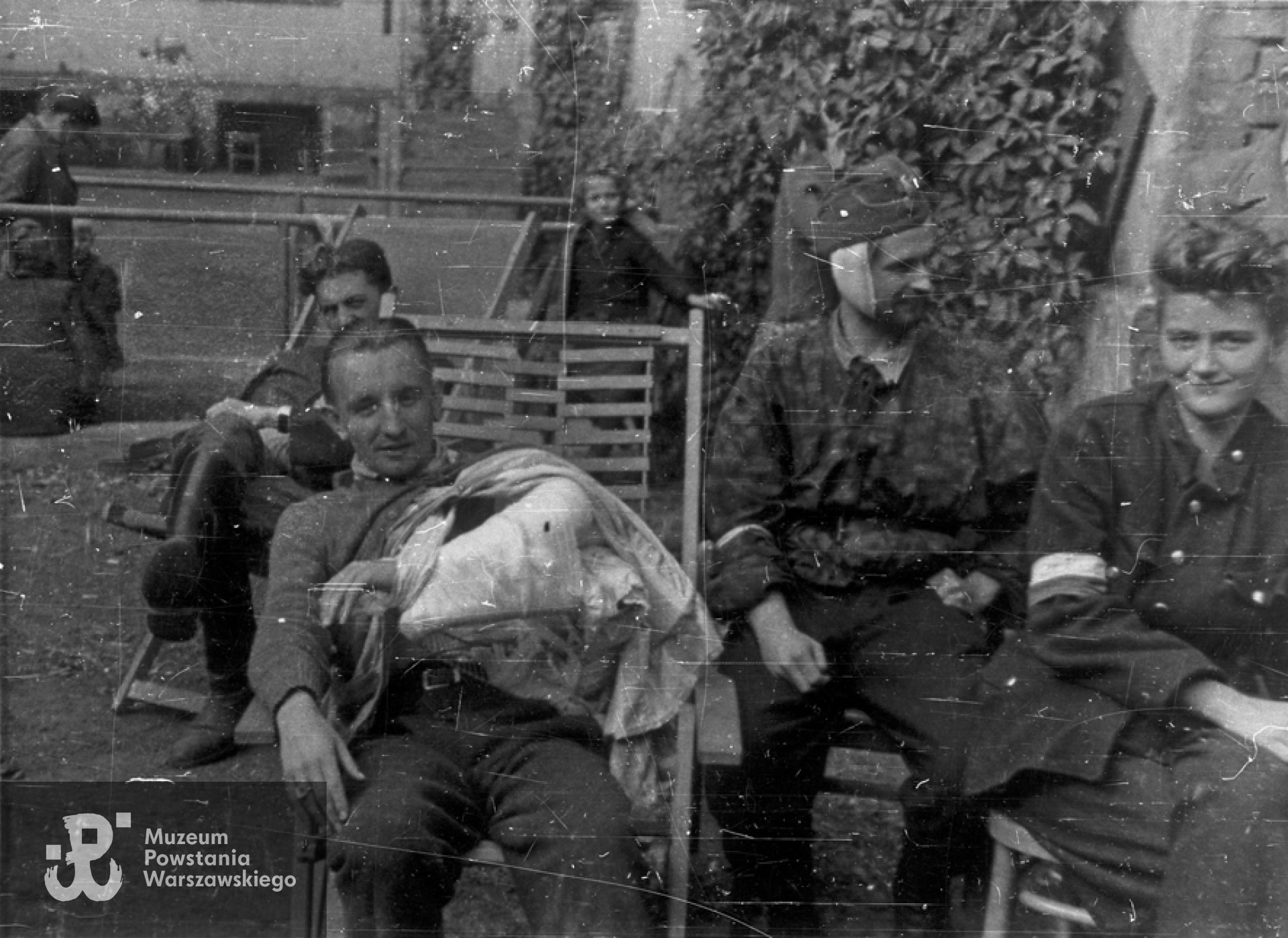 Fotografia z Powstania Warszawskiego. Śródmieście Południowe, ul. Śniadeckich. Ranni powstańcy z batalionu "Chrobry I" w szpitalu polowym  przy ul. Śniadeckich 17 (ewakuowany z ul. Senatorskiej Szpital Maltański). Drugi od lewej por. Eugeniusz Glass-Brudziński "Marek", trzeci - pchor. Stanisław Ptaszyński "Skała", pierwsza z prawej - łączniczka Krystyna Zapaśnik "Krystyna".  Autorem fotografii jest Zygmunt Sowiński "Ostoja". Ze zbiorów Muzeum Powstania warszawskiego, sygn. MPW-IN/8739