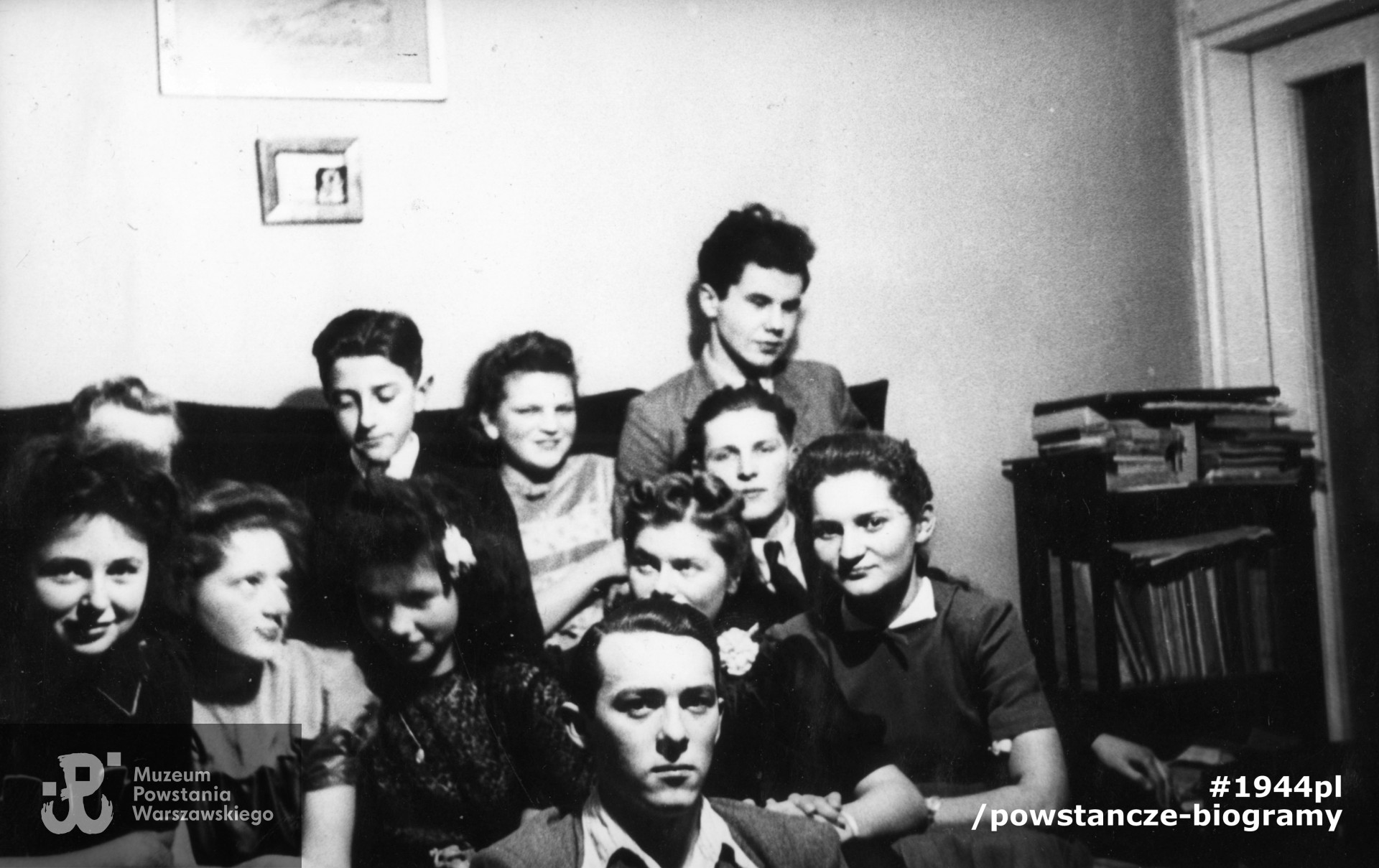 Fotografia z okresu okupacji niemieckiej. Warszawa. Grupa młodzieży żoliborskiej podczas spotkania w mieszkaniu prywatnym. Na pierwszym planie siedzi Olgierd Budrewicz, dalej od lewej: Janka Fabicka, Hanna Kamler, Anna Kanicka (z kwiatkiem we włosach), Alicja Natanson i NN. Z tyłu od lewej: Zdzisław Kwieciński (widoczny tylko fragment głowy), Wiktor Natanson, NN, Zbigniew Kryst "Wilimowski" (poległ w Akcji "Bollongino"), poniżej NN . Fot. ze zbiorów Muzeum Powstania Warszawskiego, sygn. MPW-IP/6321-165