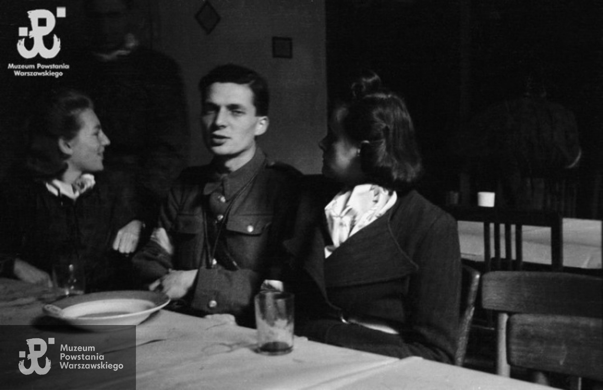 Powstanie Warszawskie, wrzesień 1944 r. Posiłek powstańców z kompanii "Anna” batalionu "Gustaw” w kwaterze przy ulicy Jasnej 19. Przy stole od lewej: Danuta Magreczyńska "Danka”, por. Wojciech Sarnecki "Wojtek”, Janina Sanecka "Roma”. Autorem zdjęcia jest Wiesław Chrzanowski. Ze zbiorów Muzeum Powstania Warszawskiego, sygn. MPW-IN/3325