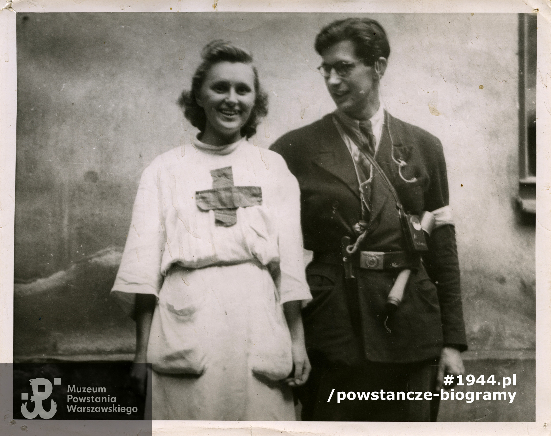 Fotografia z Powstania Warszawskiego. Śródmieście Północne. Sanitariuszka Anna Ziembińska "Hanka" i powstaniec Jerzy Cichoński "Jurek 2020" z kompani "Grażyna" na podwórzu domu przy ul. Mazowieckiej 4 (G). Fot. ze zbiorów Muzeum Powstania Warszawskiego, sygn. MPW-IP/5995.  Autorem zdjęcia jest Prasowy Sprawozdawca Wojenny (PSW) ps. "Kolec"