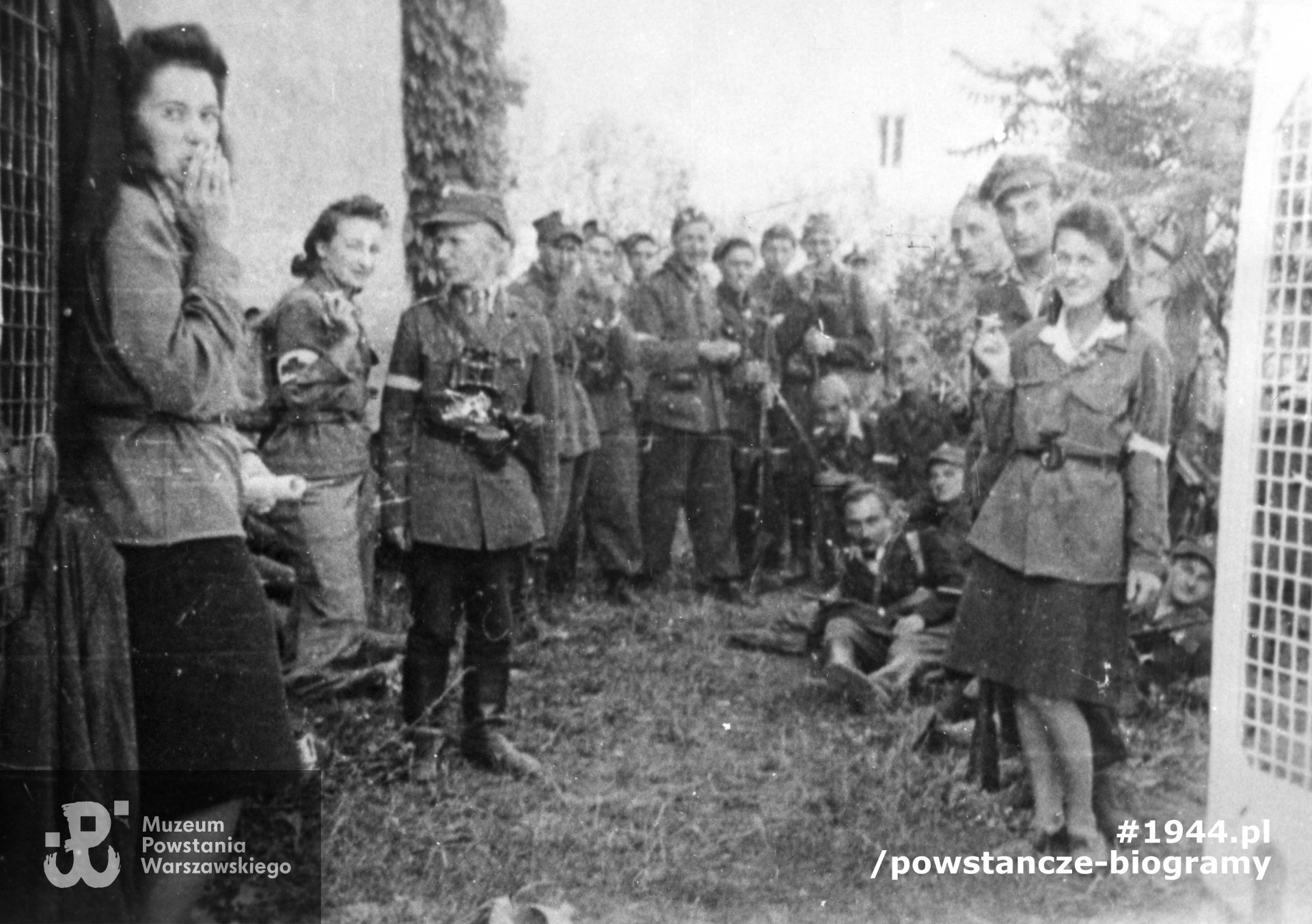 Fotografia z Powstania Warszawskiego. Żoliborz, żołnierze Zgrupowania "Żaglowiec". Na tyłach domu Mickiewicza 11 róg ul. Zajączka (podwórko). Od lewej: sanit. Hanna Filipowicz "Hanka", sanit. Izabella Czerwcowa "Jolanta", "Iza" (zamordowana przez Niemców po zakończeniu Powstania), ppor. Edward Redel "Lot" - zastępca dowódcy plut. 207. Od prawej: sanit. Danuta Kędzierska "Danka", kpr. pchor. Albert Paszkowski "Ben", plut. pchor. Witold Poniatowski "Chrobotek". W głębi nierozpoznani żołnierze plut. 207. Fot. ze zbiorów Muzeum Powstania Warszawskiego, sygn. MPW-IP/5435