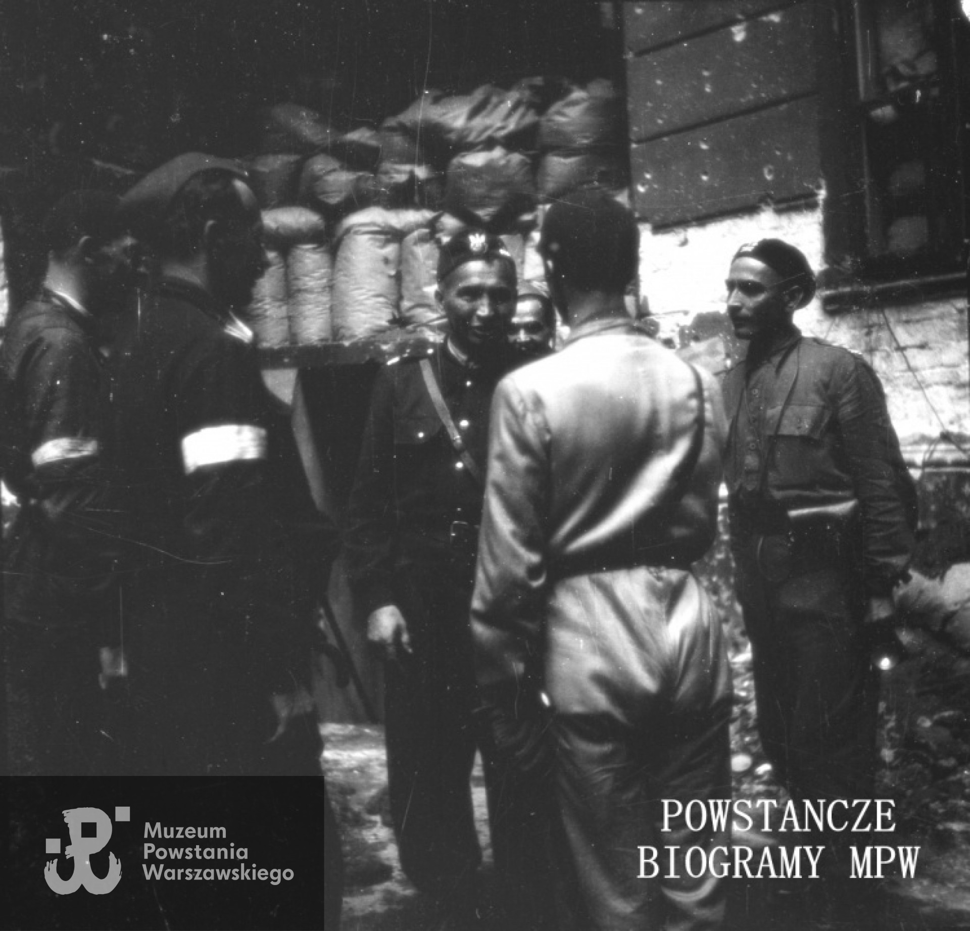 Fotografia z Powstania Warszawskiego autorstwa Jerzego Einhorna ps. "Sław". Śródmieście Południowe, ul. Poznańska 12. Generał Leopold Okulicki "Niedźwiadek" (drugi z prawej) podczas inspekcji na placówce Batalionu "Zaremba-Piorun", dowodzonego przez kpt. Franciszka Malika "Pioruna".  Fot. ze zbiorów Muzeum Powstania Warszawskiego, sygn. MPW-IN/9035