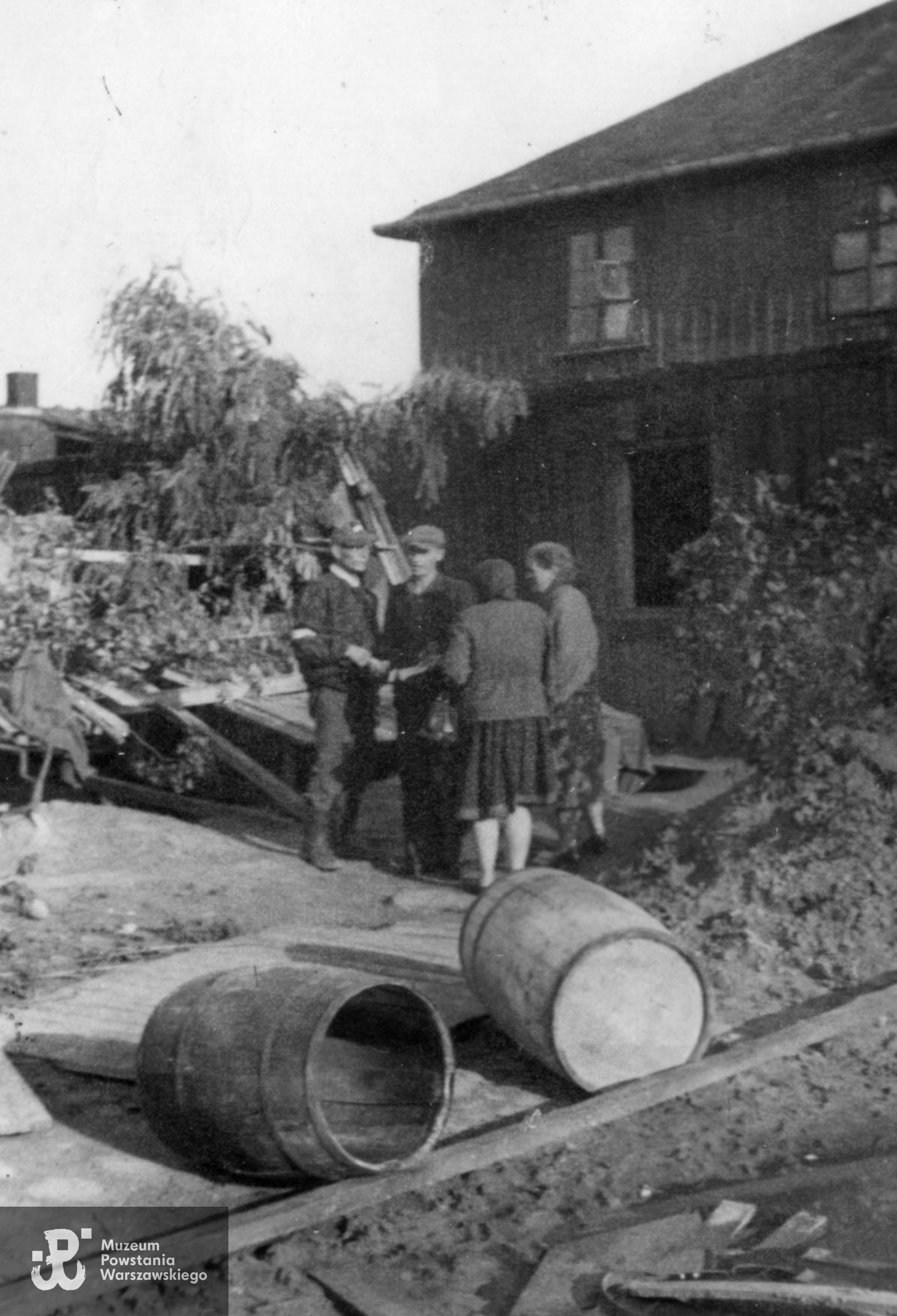 Fotografia z Powstania Warszawskiego, której autorem jest Wiesław Ganin "Gil":  na zdjęciu Powstańcy rozmawiający na z kobietami przy umocnieniu z piasku i beczek wzniesionym na posesji Młynarska 31 na Woli. Początek sierpnia 1944 roku. Fot. ze zbiorów Muzeum Powstania Warszawskiego, sygn.  MPW-IP/6684 (P/7775/13)