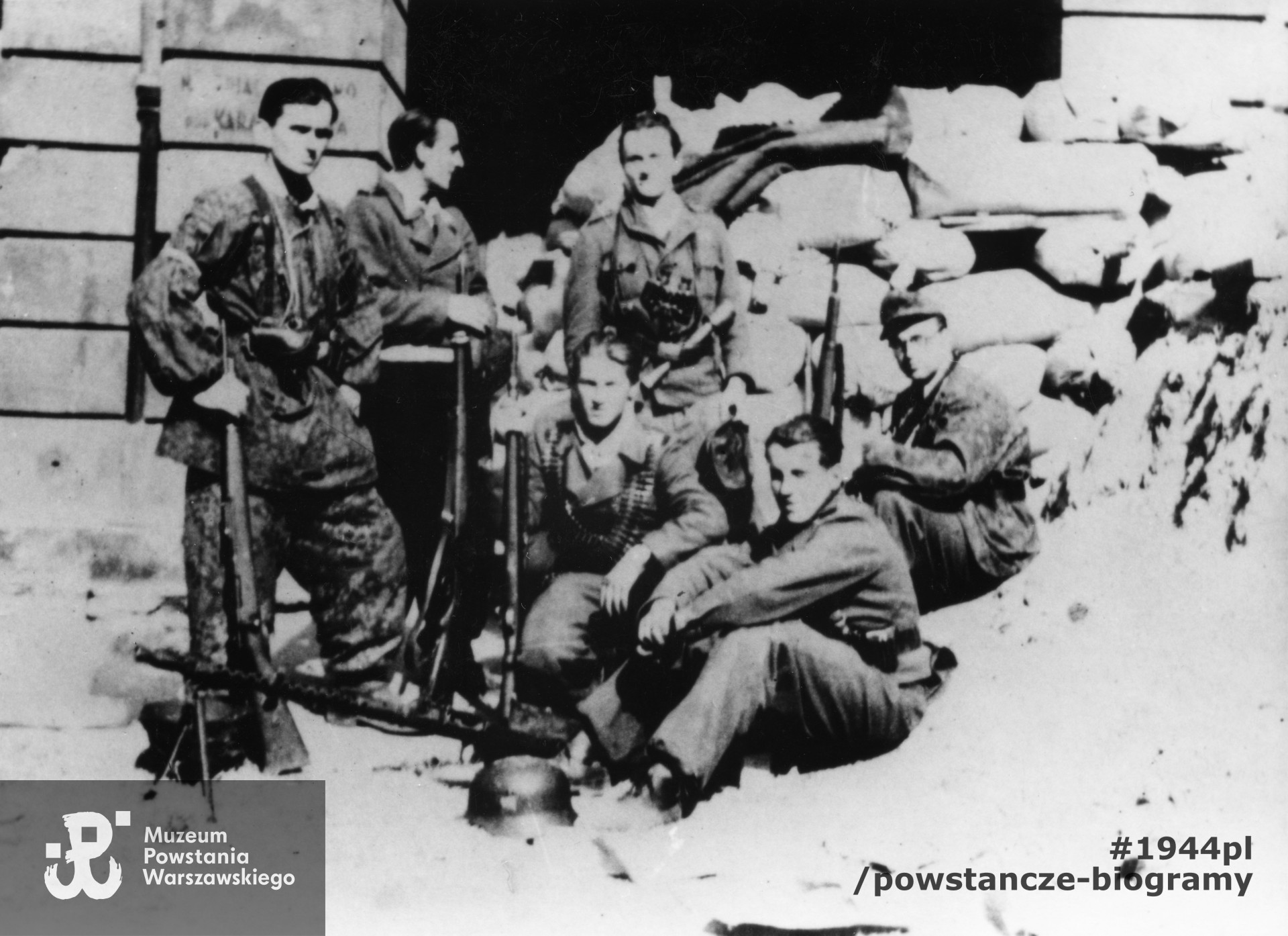 Fotografia z Powstania Warszawskiego. Śródmieście Północne. Powstańcy z Kompanii wypadowej kpt. "Prusa", batalionu "Gozdawa" przed bramą kamienicy przy ul. Brackiej 20. Stoją od lewej Edwin Patyna [?] "Trefll", Bogdan Kapella "Kosma" Zbigniew Ławczak "Karo". Siedzą od lewej: Tadeusz Majewski, Feliks Jeziorek "Felek", Marian Gwiazdecki "Poręba". Fot. ze zbiorów Muzeum Powstania Warszawskiego, sygn. MPW-IP/5737