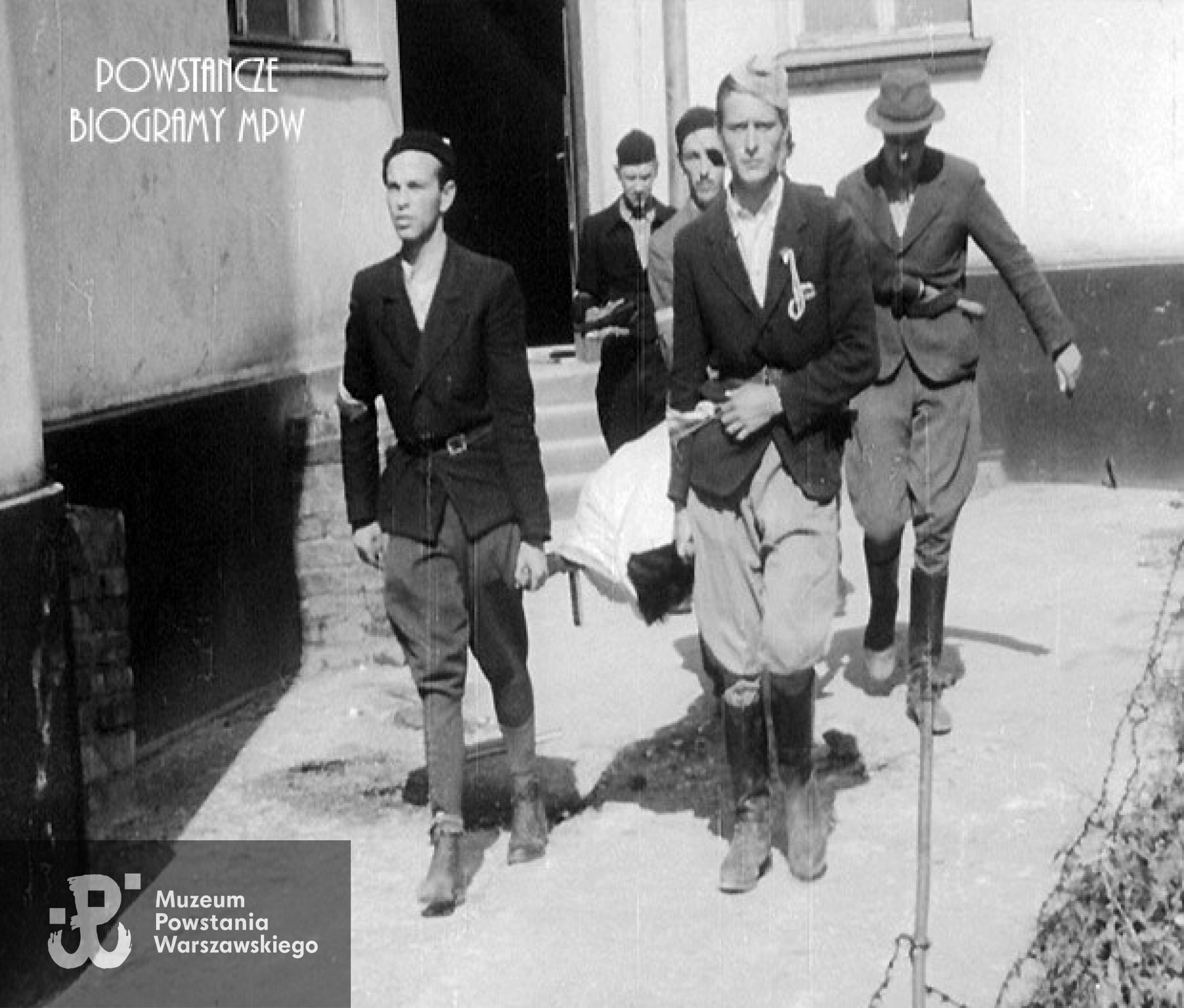 Kadr w Powstańczej kroniki filmowej. 3 sierpnia 1944. Mokotów, ulica Puławska 134 róg Naruszewicza. Wychodzący z klatki schodowej powstańcy z dywizjonu „Jeleń” niosą na noszach ciało ppor. Stanisława Jenike „Hański”, zastępcy dowódcy plutonu 1110 dywizjonu „Jeleń”. Przy noszach z przodu od lewej ułan Józef Jezierski „Aksak” i st. ułan pchor. Władysław Grabiński „Pilawa”, z tyłu od lewej kpr. pchor. Andrzej Sroczyński-Nowina „Nowak” z opaską na oku i st. ułan z cenz Paweł Mańkowski „Rapier” w kapeluszu. W tle ciemna sylwetkla ułan Wiktor Wcisło „Kmita”. Pojawiający sie w końcówce ujęcia w czapce cyklistówce NN. Źródło: MPW - "Powstanie Warszawskie Film"