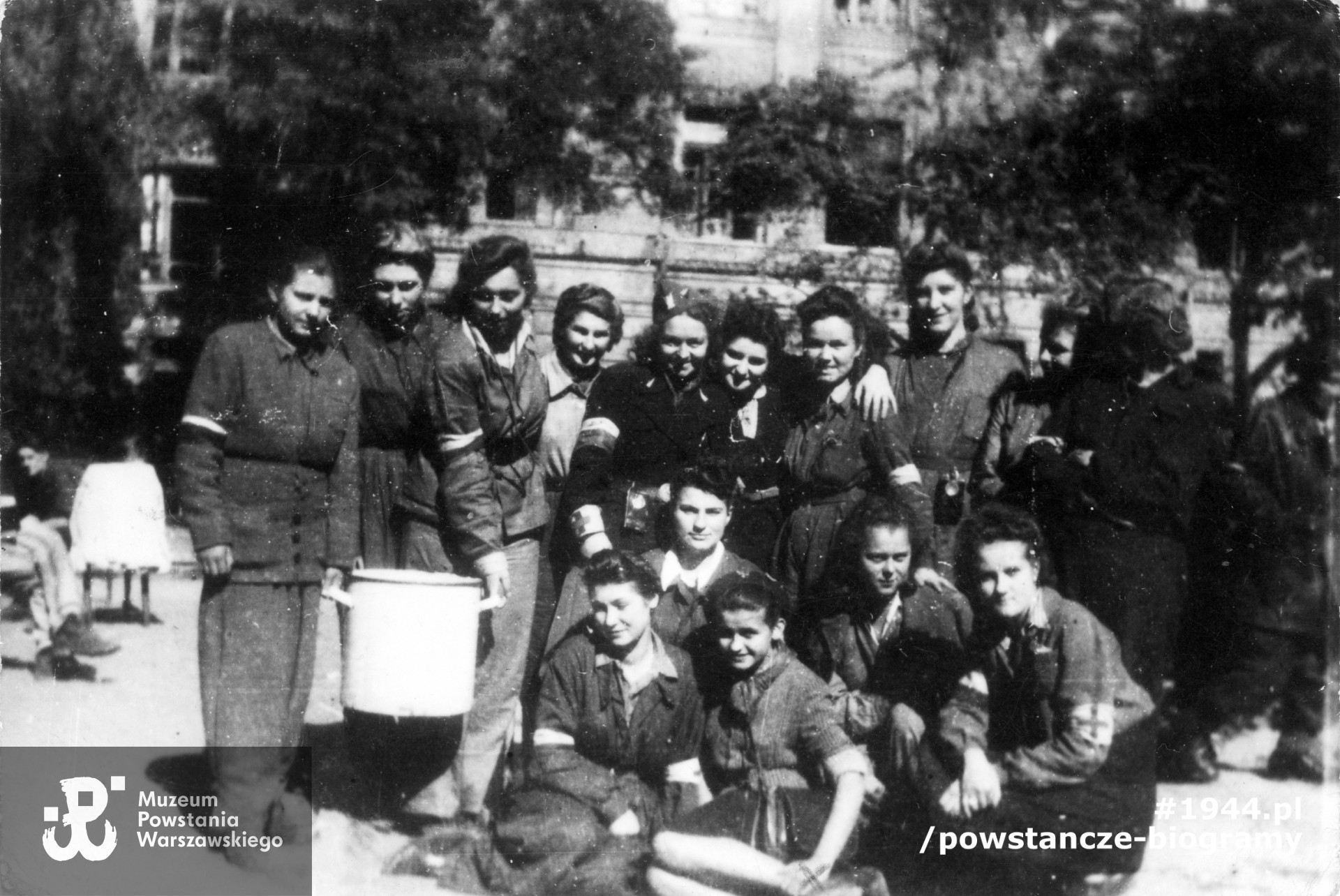 Fotografia z powstania warszawskiego. Śródmieście Południowe. Grupa łączniczek i sanitariuszek z 3. Batalionu Pancernego "Golski" na dziedzińcu Wydziału Architektury Politechniki Warszawskiej przy ul. Lwowskiej 12. Stoją od lewej: Krystyna Kunowska - Prędecka "Krysia", Krystyna Maria Grzebalska "Ksenia" [?], Jadwiga Słotwińska "Dora", Alicja Piotrowska "Krystyna", Dorota Nowicka, Katarzyna Radlińska [?], Blanka Mayer - Malesa "Jadwiga", Hanna Lewicka [?]. Siedzą od lewej: Stella Klewek "Dąbska", Aleksandra Hurtych "Lala", NN, Lidia Dürr "Kora", Krystyna Klaczyńska - Przyjemska "Awionetka" z opaską z krzyżykiem. Fot. ze zbiorów Muzeum Powstania Warszawskiego, sygn. MPW-IP/5903