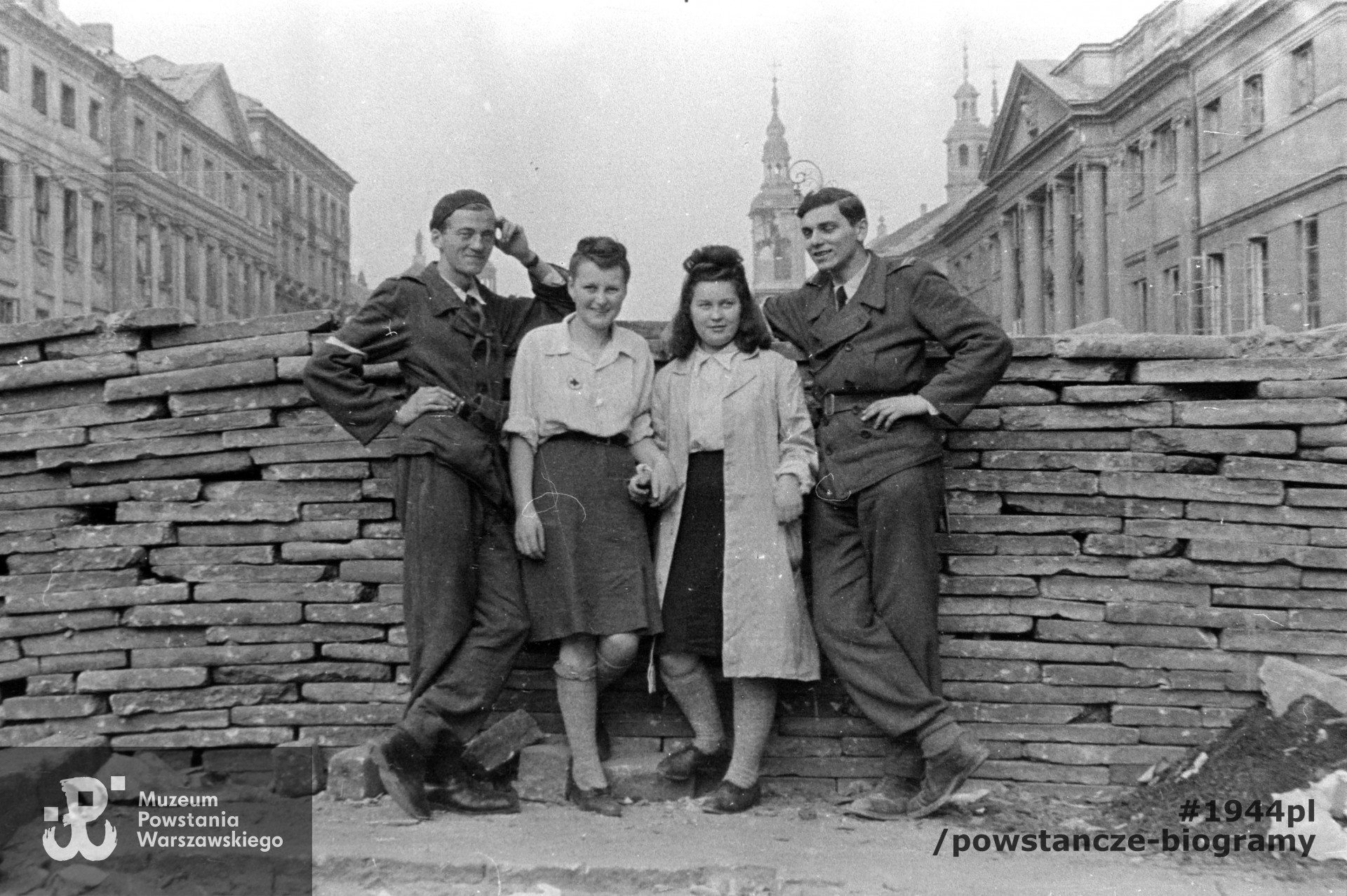 Fotografia z Powstania Warszawskiego. Starówka. Czwórka powstańców przy barykadzie przecinającej ul. Długą na wysokości wylotu ul. Kilińskiego. Pośrodku dwie kobiety w tym sanitariuszka w w jasnej bluzce z przyszytym znakiem Czerwonego Krzyża Pierwszy z lewej plut. pchor. Sebastian Maria Niewiadomski "Seb" z kompanii "Anna" Batalionu "Gustaw" (od 7 sierpnia dowódca  3 kompanii "Gertruda" tego batalionu) z widoczną na prawym ramieniu biało-czerwoną opaską. Pierwszy z prawej kpr. pchor. Roman Patynowski "Roma" z tego samego oddziału w kurtce z naszytymi pagonami. Ujęcie w kierunku północno-wschodnim. W tle od lewej: kamienica Długa 8, Długa 8a, Długa 4 i fasada kościoła dominikanów - Freta 10/8; od prawej: pałac Raczyńskich - Długa 7, Długa 5, kościół paulinów p.w. św. Ducha - Długa 3 i kamienica Freta 4.F ot. ze zbiorów Muzeum Powstania Warszawskiego, sygn. MPW-IN/11095, ujęcie tożsame MPW-IH/438. Autorem zdjęcia jest Dariusz Celiński.