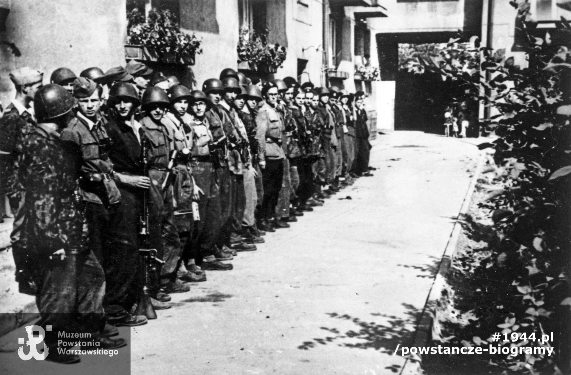 Fotografia z Powstania Warszawskiego. Żoliborz, żołnierze zgrupowania "Żyrafa". Zbiórka plutonu 227 na podwórzu bloku przy ul. Krasińskiego 20. Pierwszy od lewej w furażerce: Andrzej Ryttel "Jędrek", za nim: Andrzej Jachimczyk "Azjata", Stefan Zadróżny "Witek", Andrzej Kowalski "Sidol", w okularach Jerzy Zawadowski "Tytus", Daniel Olędzki "Kukułka". W środku w jasnej kurtce i okularach, Ryszard Witrzenc "Wacek". Autorem zdjęcia jest Mieczysław Łokcikowski "Hanibal". Fot. ze zbiorów  Muzeum Powstania Warszawskiego, sygn. MPW-IH/599
