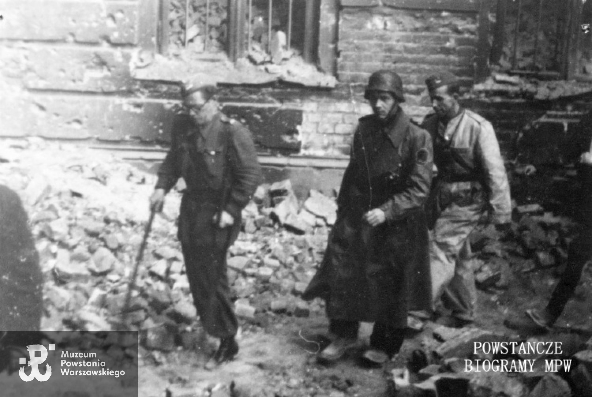 Zdjęcie filmowe z okresu Powstania Warszawskiego autorstwa Stefana Bagińskiego: Śródmieście Południowe, Powstańcy z batalionu KB "Sokół" idący na rozmowy w sprawie miejscowego zawieszenia broni. O kulach na jednej nodze mjr Eugeniusz Morozowicz "Janek" z-ca dowódcy batalionu. Widoczni także: ppor. „Patriota” (Zygmunt Królak) i  por. „Skała” (Alfons Laska). Fot. ze zbiorów Muzeum Powstania Warszawskiego, sygn.  MPW-IP/1932