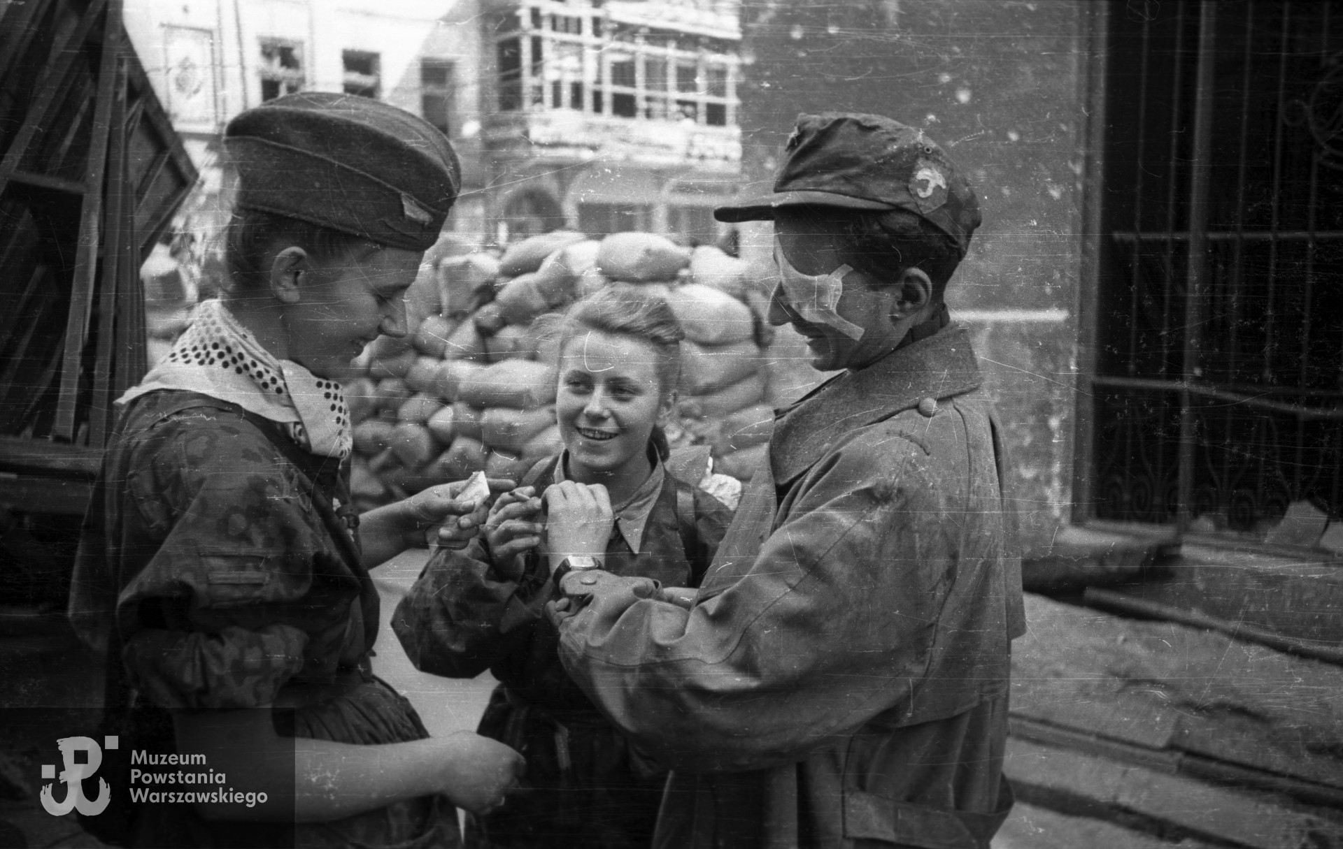 Fotografia z Powstania Warszawskiego. Śródmieście Północne. Sanitariuszka NN i ranny Krzysztof Palester "Krzych" z batalionu "Parasol" po wyjściu z kanałów na ul. Wareckiej przy Nowym Świecie. W środku stoi Maria Stypułkowska-Chojecka "Kama". Fot. Joachim Joachimczyk. Ze zbiorów Muzeum Powstania Warszawskiego, sygn. MPW-IN/10737.