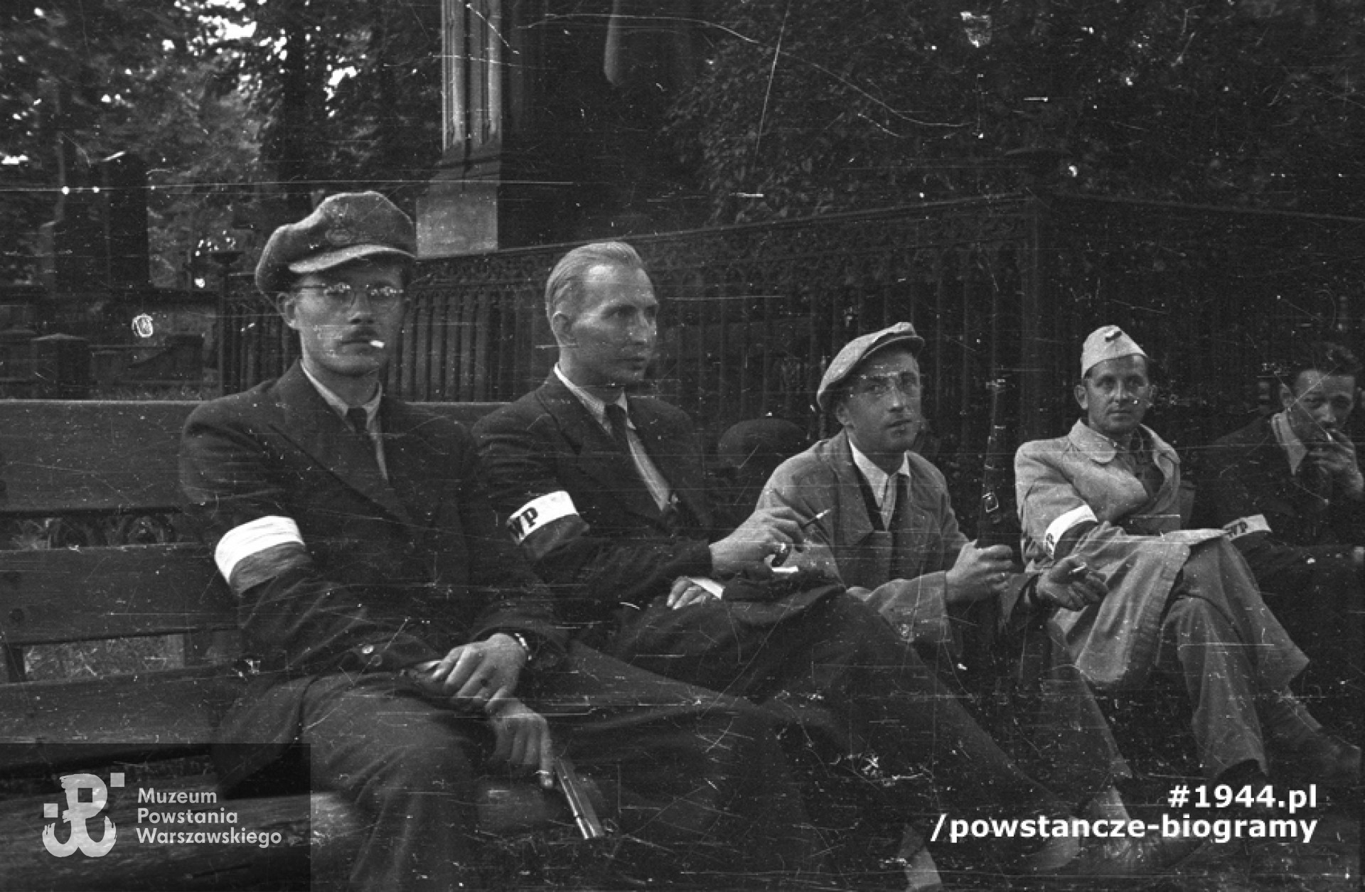 Fotografia z Powstania Warszawskiego. Wola. Godzina "W". Koncentracja powstańców z plutonu "Agaton" Batalionu "Pięść" na cmentarzu ewangelicko-augsburskim. Pierwszy z lewej siedzi Stefan Bałuk "Kubuś", obok niego kpr. Seweryn Brwiliński "Adam". Fot. ze zbiorów Muzeum Powstania Warszawskiego, sygn. MPW-IS/120