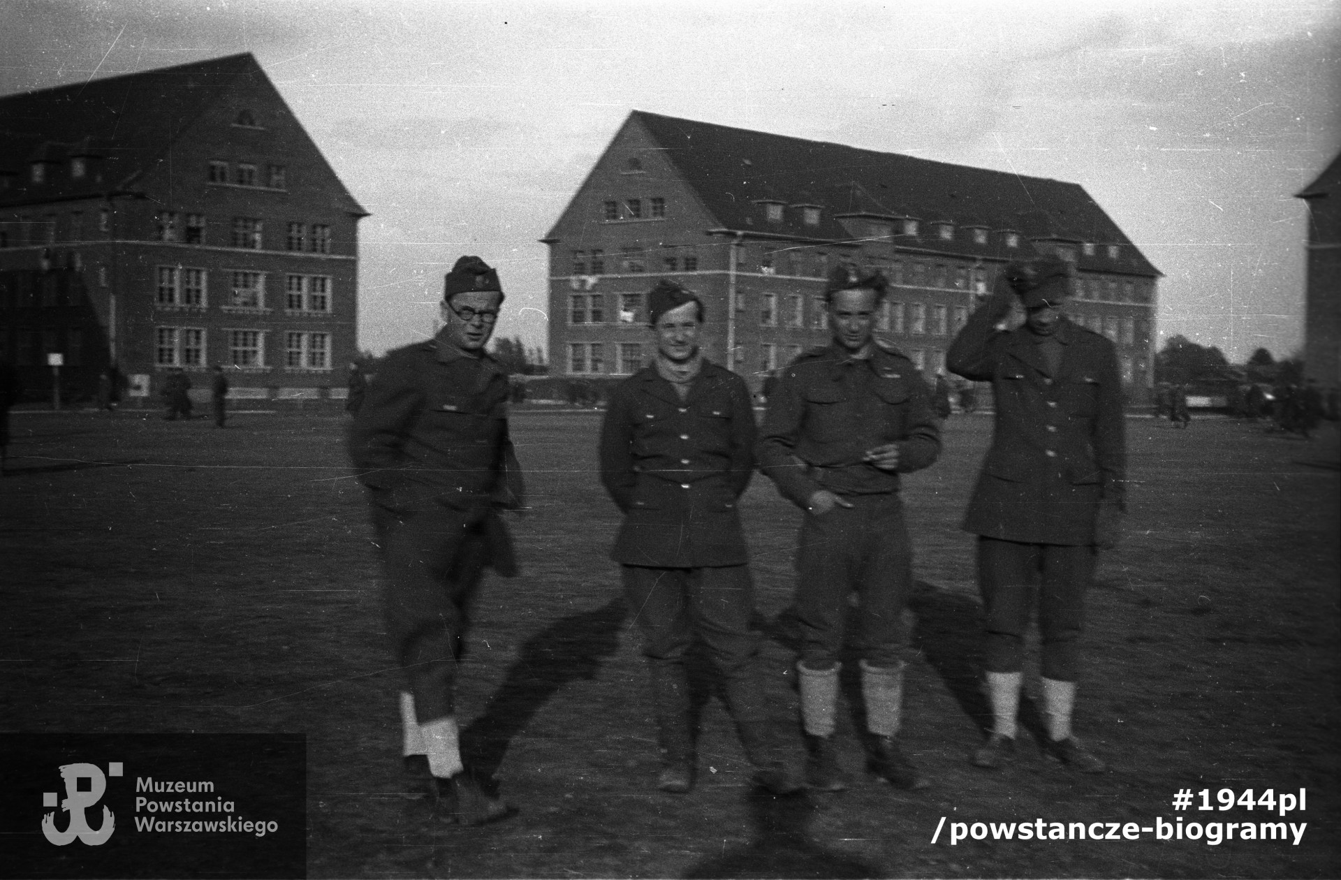 Fotografia z Oflagu X C w Lubece. Grupa polskich oficerów na placu przez blokami koszarowymi. Od lewej stoją: ppor. Henryk Ożarek "Henio" z kompanii "Anna" Batalionu "Gustaw", kpr. pchor. Wojciech Bogusławski "Tur", ppor. Stefan Mączyński "Szczepcio" z kompanii "Harcerskiej" Batalionu "Gustaw", ppor. Kazimierz Skrobik "Koń" z kompanii "Janusz" Batalionu "Harnaś". Ze zbiorów Muzeum Powstania Warszawskiego, sygn. MPW-IN/3401, kolekcja Wiesława Chrzanowskiego "Wiesław"
