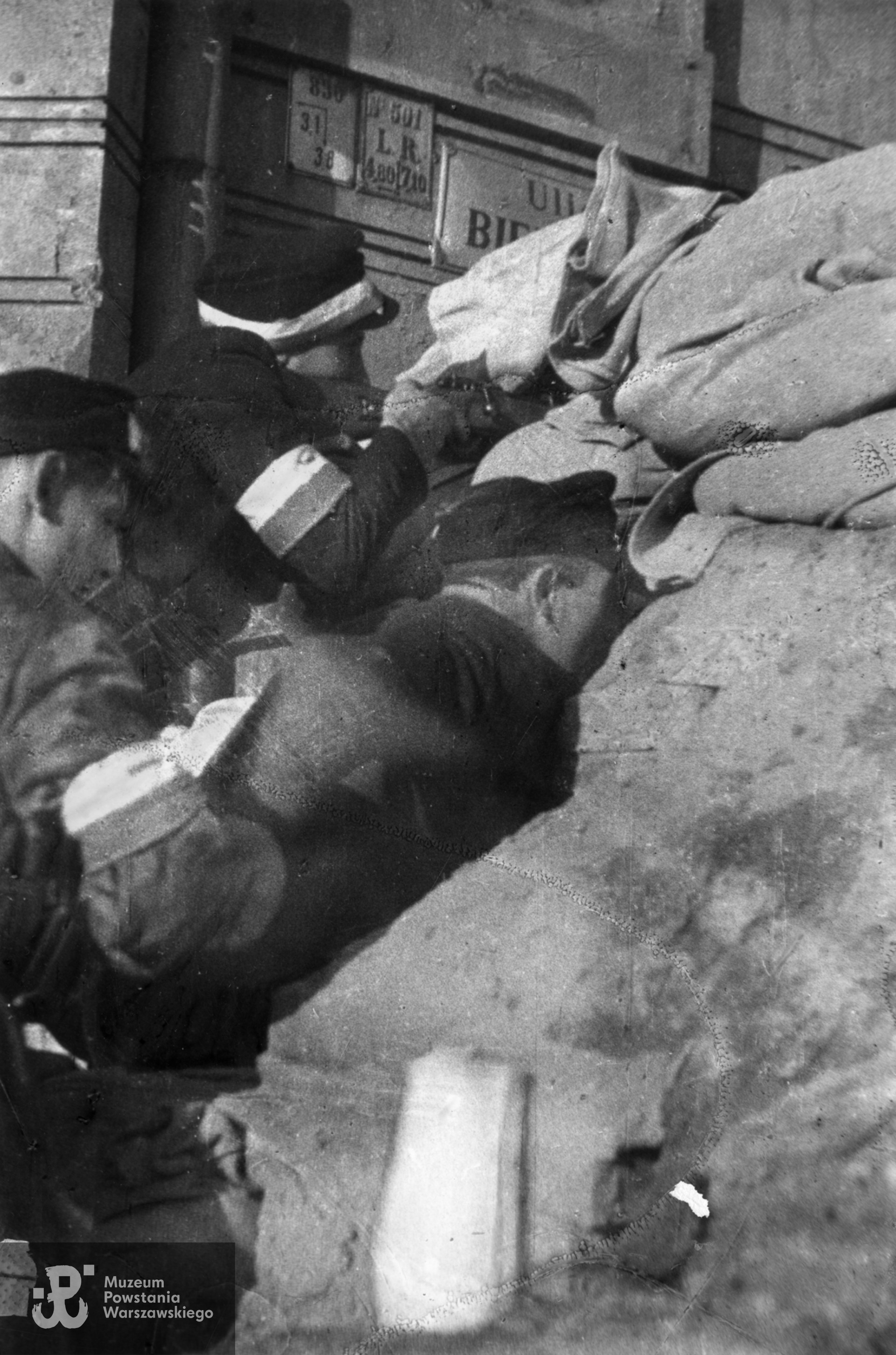 Fotografia z Powstania Warszawskiego Starówka. Powstańcy na barykadzie "Żyrardów", zwanej też redutą "św. Trójcy" przegradzającej ul. Bielańską na wysokości wylotu ul. Daniłowiczowskiej. W tle po prawej widoczny fragment elewacji dawnego Hotelu Lipskiego przy ul. Bielańskiej 3. Autorem zdjęcia jest Józef Jerzy Karpiński. Fot. ze zbiorów Muzeum Powstania Warszawskiego, sygn. MPW-IP/6483