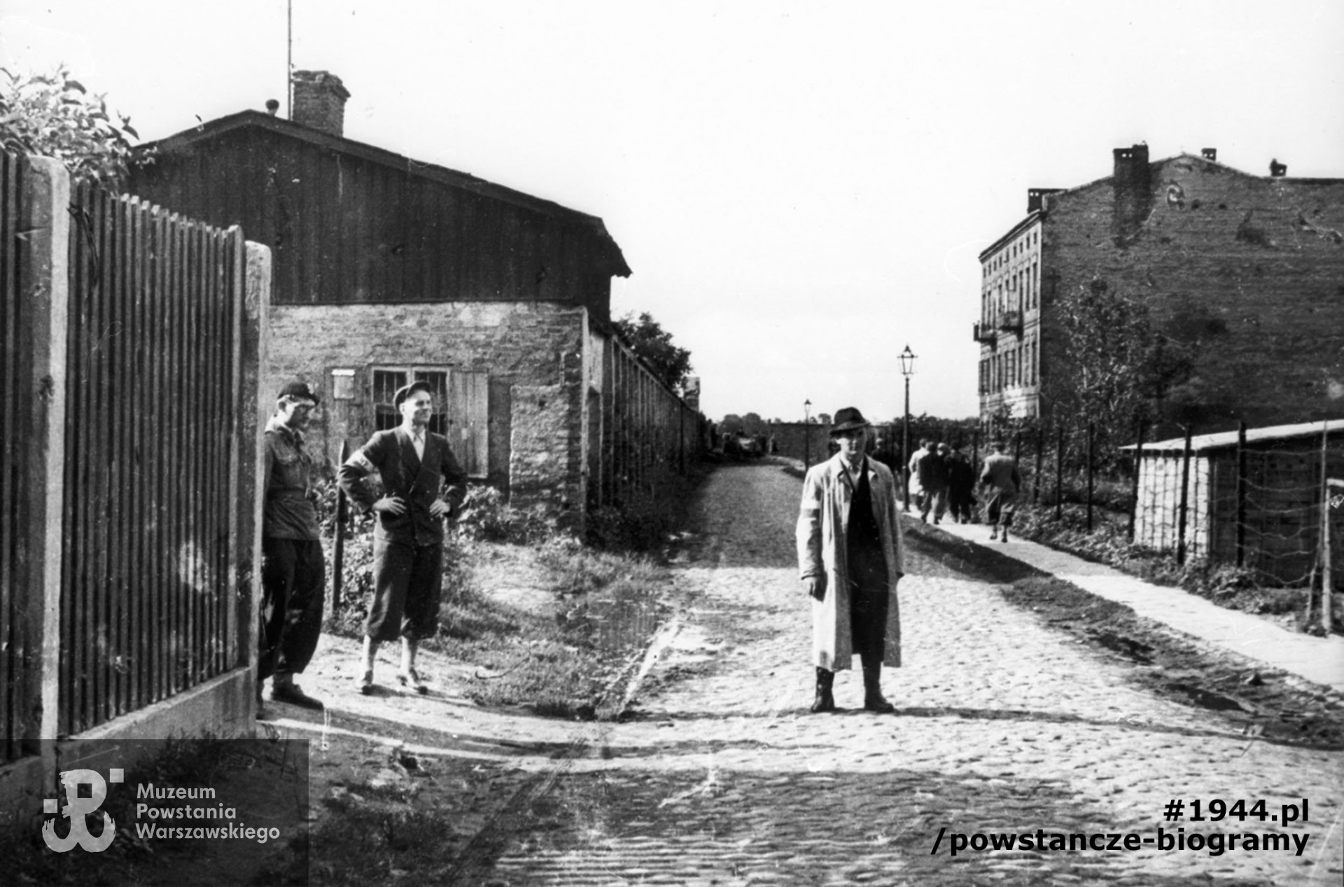  Wola. Godzina "W". Grupa powstańców z Batalionu "Pięść" stojąca przy wylocie ul. Długosza na ul. Karolkową, w oczekiwaniu na koncentrację oddziału. Widoczna perspektywa ul. Karolkowej w kierunku północnym. Od lewej stoją: kpr. (NN), mjr Alfons Kotowski "Okoń", dowódca Batalionu i ppor. Stanisław Bąk "Burza" (w jasnym płaszczu). Autorem zdjęcia jest Stefan Bałuk. Ze zbiorów Muzeum Powstania Warszawskiego, sygn. MPW-IH/3406. Prawa autorskie MPW