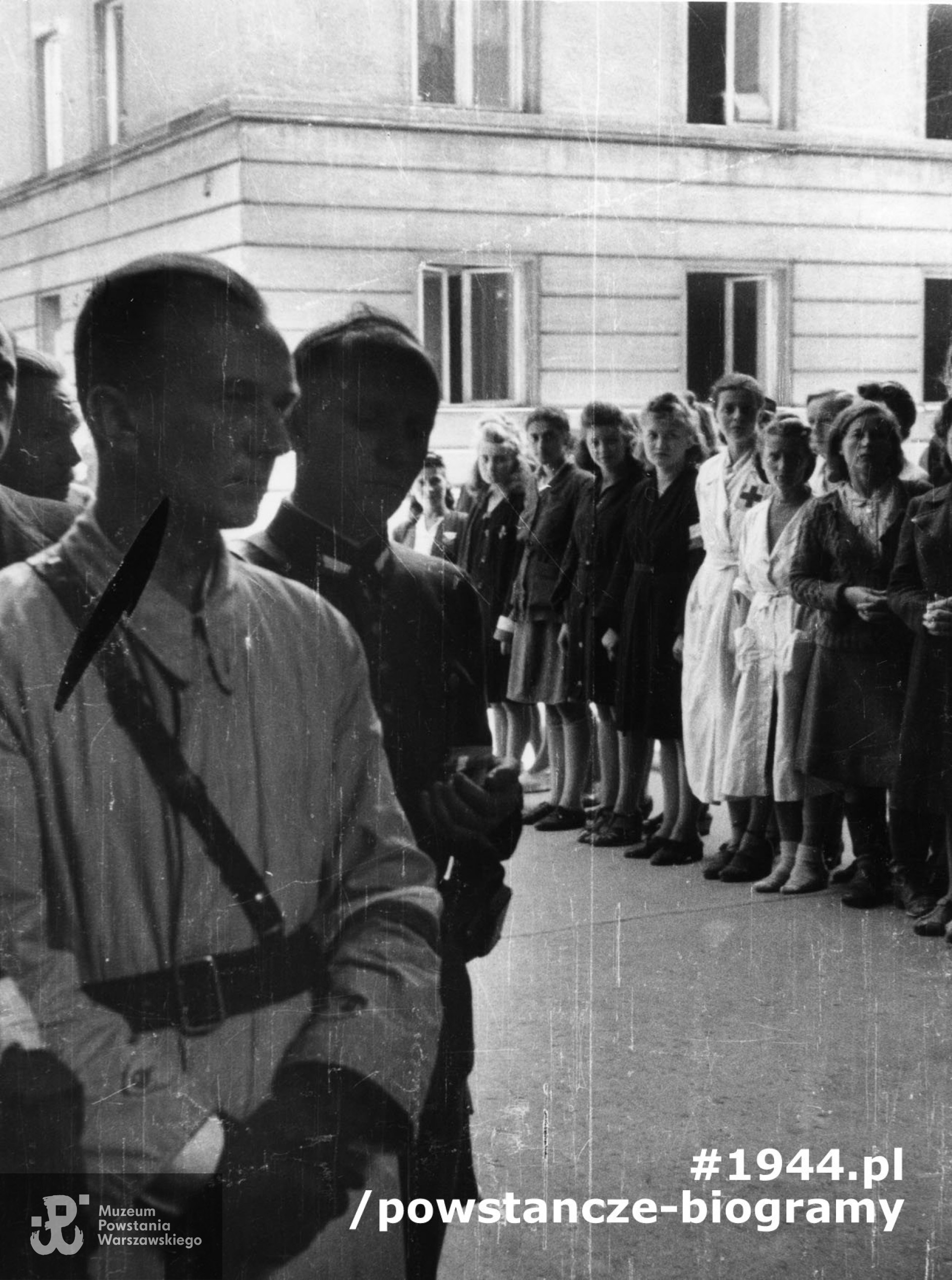 Fotografia z Powstania Warszawskiego. Powiśle. Msza polowa odprawiana w bramie gmachu przy ul. Smulikowskiego 1/3, gdzie przed wojną mieściła się Bursa ZNP. Pierwszy z lewej kpt. Juliusz Szawdyn „Konrad”, dowódca III Zgrupowania „Konrad” Grupy Bojowej „Krybar” AK, obok prawdopodobnie kpt. Stanisław Krowacki „Leonowicz”.  W tle widoczne w białych fartuchach - siostra Janina - Janina Burska po  mężu Toborowicz oraz Maria Piotrowicz ps. „Irena„. Fot. ze zbiorów Muzeum Powstania Warszawskiego, sygn. MPW-IK/1609. Identyfikacja ”Janiny„ i ”Ireny" - p. Piotr Toborowicz.