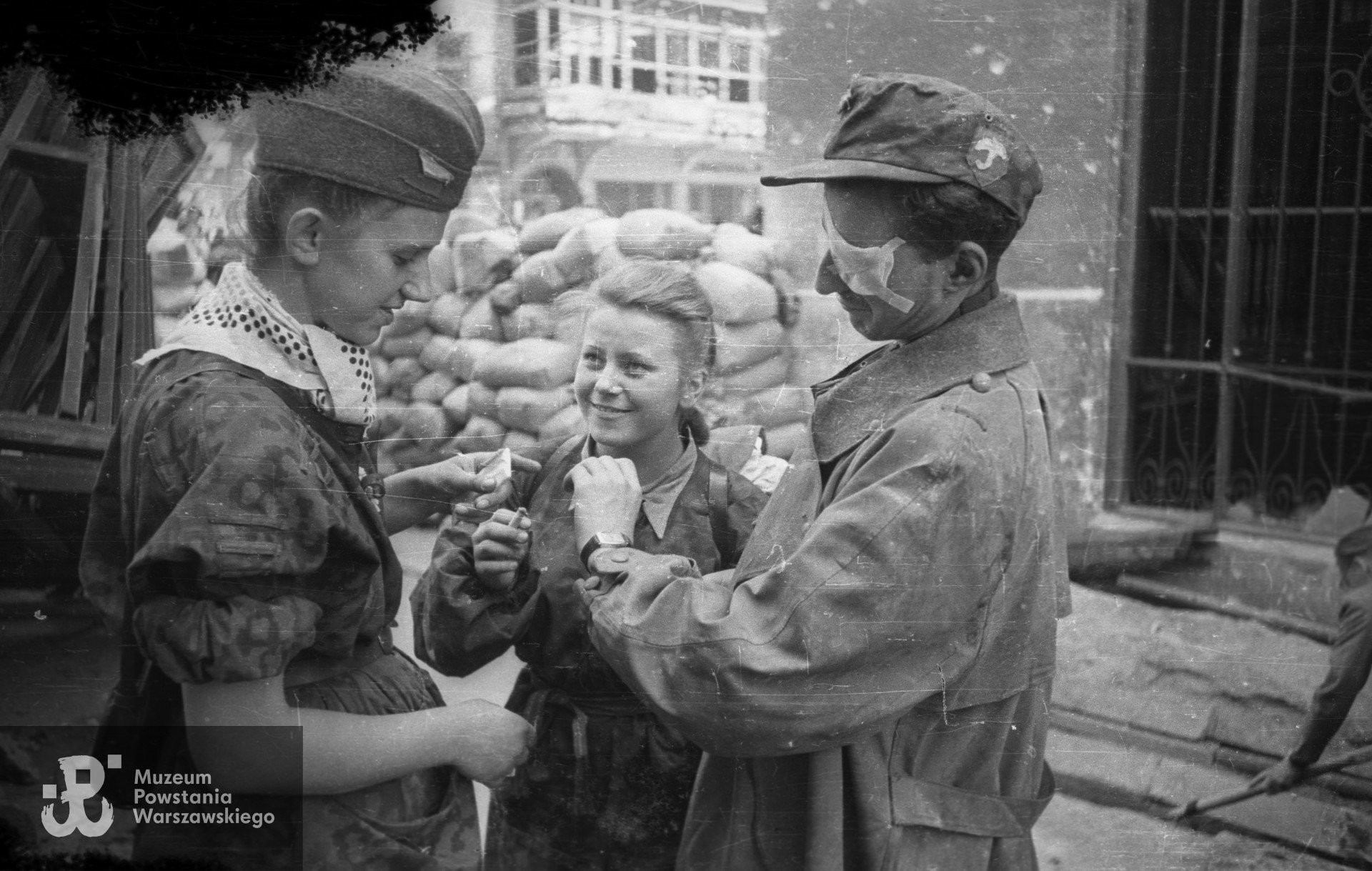 Fotografia z Powstania Warszawskiego. Śródmieście Północne. Sanitariuszka NN i ranny Krzysztof Palester "Krzych" z batalionu "Parasol" po wyjściu z kanałów na ul. Wareckiej przy Nowym Świecie. W środku stoi Maria Stypułkowska-Chojecka "Kama". Fot. Joachim Joachimczyk. Ze zbiorów Muzeum Powstania Warszawskiego, sygn. MPW-IN/10736.