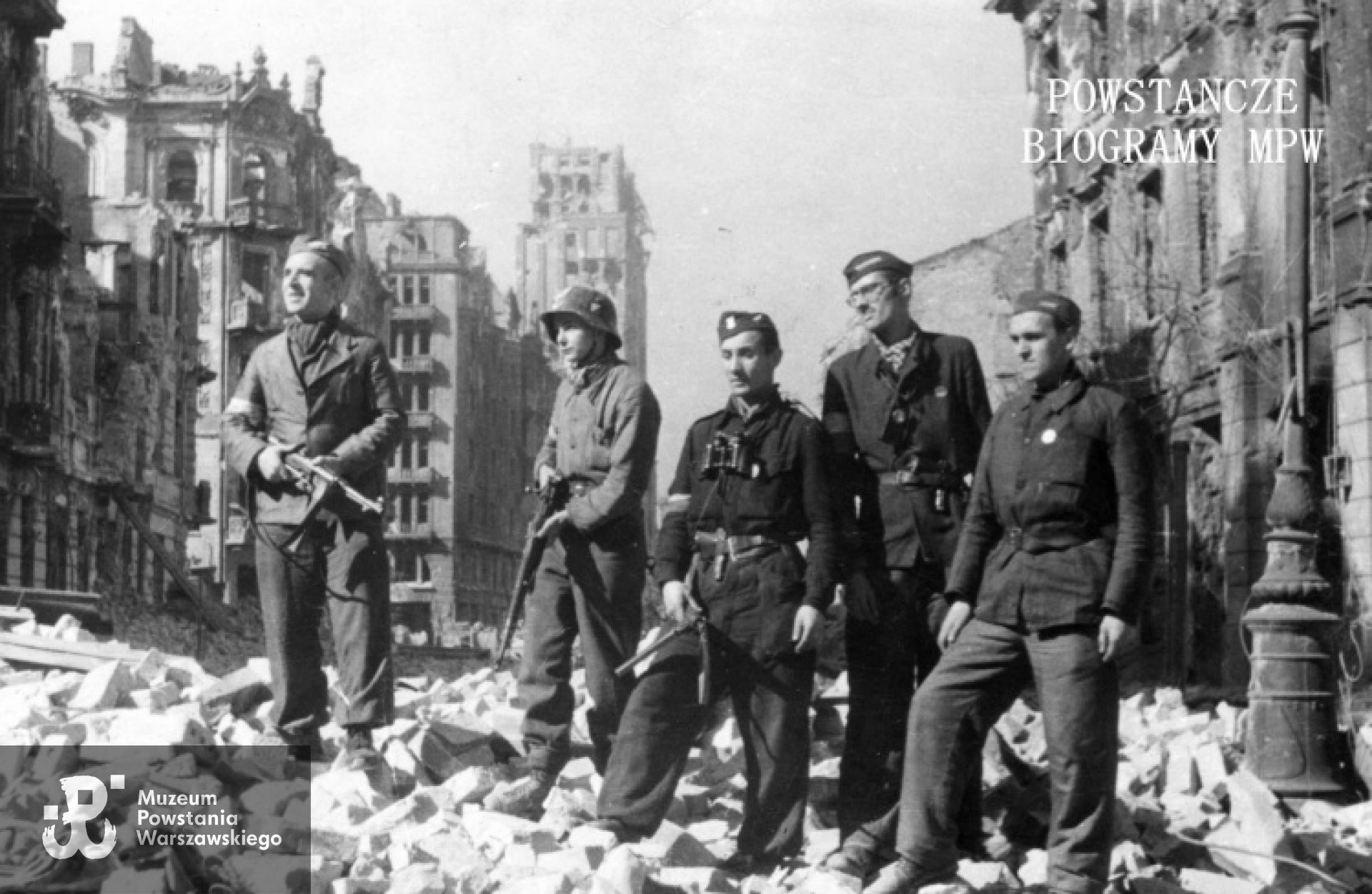 Powstanie Warszawskie. Śródmieście Północne. ul. Szpitalna. Zdjęcie grupowe  powstańców z III zgrupowania "Konrad". W tle ruiny ulicy Szpitalnej i gmachu Prudentialu. Kpr. pchor. Janusz Paszyński ps. "Machnicki" stoi drugi od prawej. Fot. ze zbiorów Muzeum Powstania Warszawskiego, sygn. MPW-IP/2145