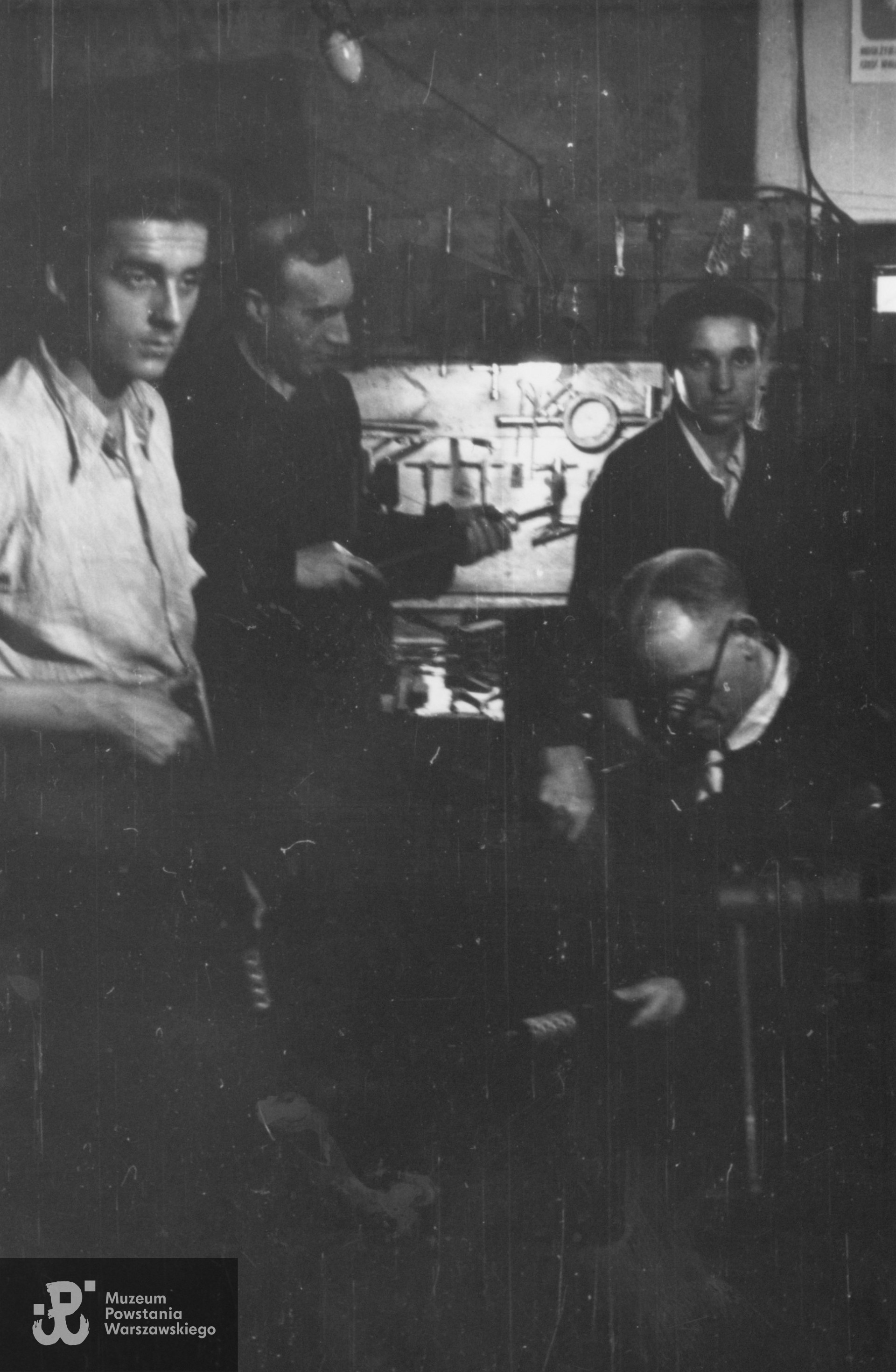 Fotografia z Powstania Warszawskiego. Śródmieście Północne. Montownia pistoletów maszynowych Błyskawica w kamienicy Lewenfisza przy pl. Napoleona 1, róg Boduena 2, róg Sienkiewicza 1. Rusznikarze Oddziału Osłonowego Wojskowych Zakładów Wydawniczych (WZW) przy pracy. Po lewej NN i st. wachm. Roch Kafarowski "Ksawery", po prawej siedzi sierż. Roman Brzosko "Szpak", za nim jego syn Stanisław.  Fot. ze zbiorów Muzeum Powstania Warszawskiego, sygn. P/7958, ujęcie tożsame: MPW-IN/369. Autorem zdjęcia jest Eugeniusz Lokajski "Brok"