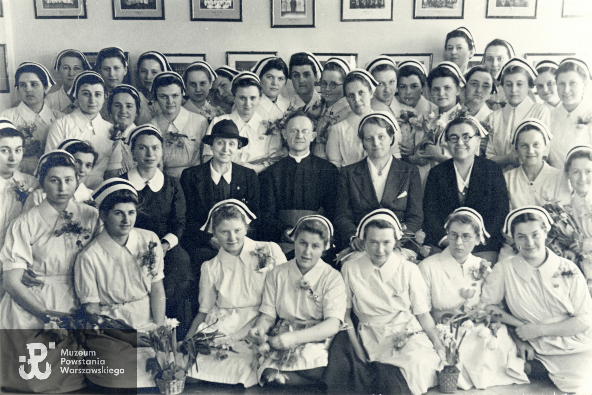 Absolwentki Warszawskiej Szkoły Pielęgniarstwa, 1943 rok. W środku grono pedagogiczne, od lewej Małgorzata Żmudzka (1883-1944), przedwojenna instruktorka Warszawskiej Szkoły Pielęgniarstwa, do 1943 roku dyrektorka Szkoły Pielęgniarstwa PCK w Warszawie  na ul. Smolnej 6 (połączonej przez Niemców w 1943 z WSP na Koszykowej 78), ks. płk Tadeusz Julian Jachimowski, naczelny kapelan ZWZ-AK oraz  kapelan Warszawskiej Szkoły Pielęgniarstwa przy ul. Koszykowej 78, obok niego Jadwiga Romanowska, dyrektorka szkoły, następnie wicedyrektorka Wanda Lankajtes. Wśród absolwentek stojących za pedagogami, na lewo od Małgorzaty Żmudzkiej widoczna jest piel. Feliksa Tomaszewska ps. Elipsa. Fot. ze zbiorów rodzinnych, udostępnili p. Jacek Krzysztof Moskwa i p. Stanisława Piotr Moskwa, synowie piel. Feliksy Tomaszewskiej. Skany wykonano w Muzeum Powstania Warszawskiego, 03/2024