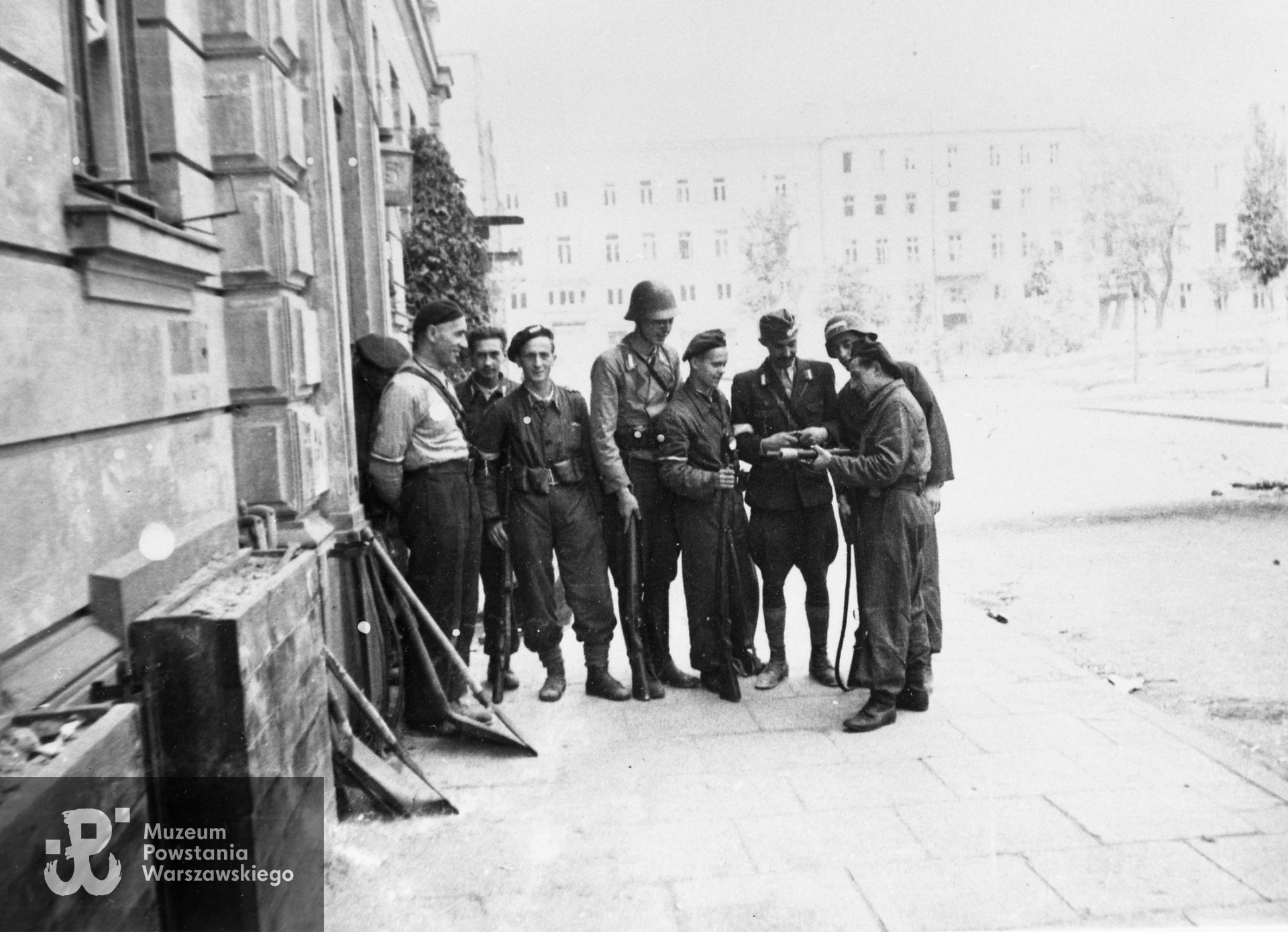 Fotografia z Powstania Warszawskiego. Śródmieście Północne. Dowódca plutonu 1150 por. Władysław Darmosz "Kutno" (trzeci od prawej) wśród swoich żołnierzy przed kwaterą na pl. Dąbrowskiego 5. Ujęcie w kierunku północnym. Autorem zdjęcia jest Joachim Joachimczyk. Fot. ze zbiorów Muzeum Powstania Warszawskiego,  sygn.  MPW-IH/4860