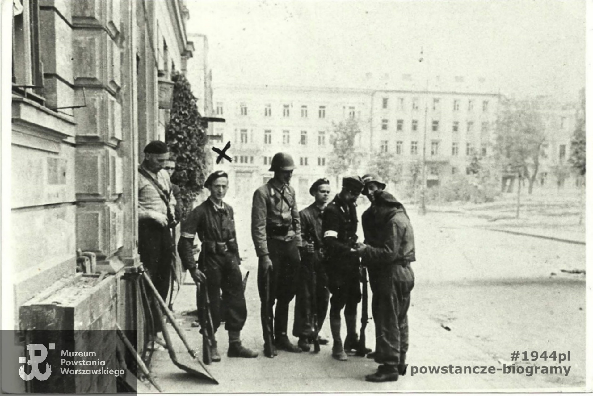 Śródmieście Północne. Pięciu żołnierzy 1150 plut. Zgrupowania „Bartkiewicz” (trzej uzbrojeni z karabiny) przed swoją kwaterą na pl. Dąbrowskiego 5, połowa sierpnia 1944. Fot. ze zbiorów rodzinnych - kpr. pchor.  Józef Rumiński „Spartanin"  zaznaczony "X". Fot. udostępnił p. Jarosław Tomasz Sobczak, zięć. Ujęcie tożsame w zbiorach MPW: MPW-IP/2467
