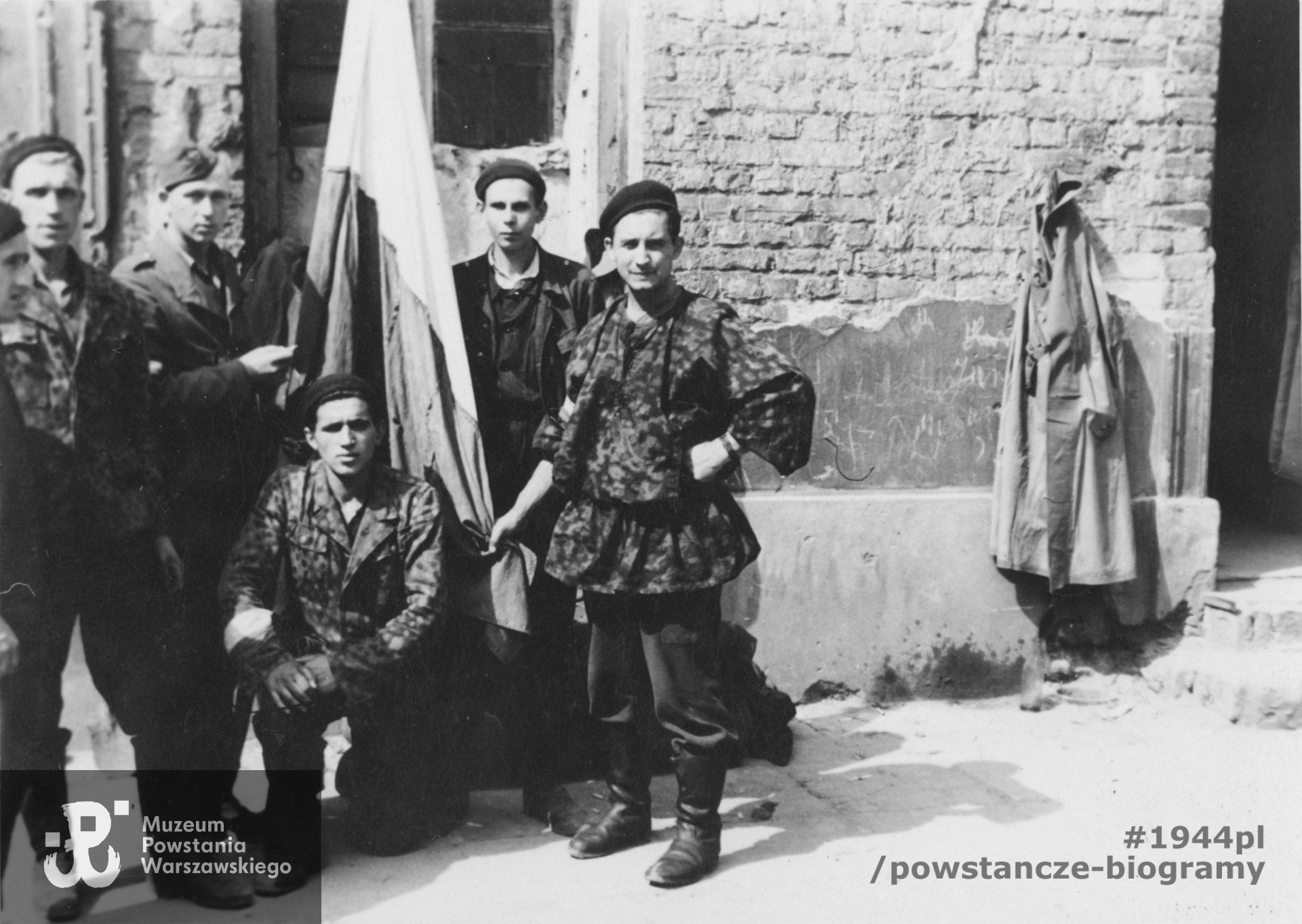 Fotografia z Powstania Warszawskiego przedstawiająca grupę Powstańców na Starym Mieście.  Flagę trzyma Alfons Milewczyk. Fot. ze zbiorów Muzeum Powstania Warszawskiego, sygn. P/9079, dar p. Krzysztofa Jaworskiego