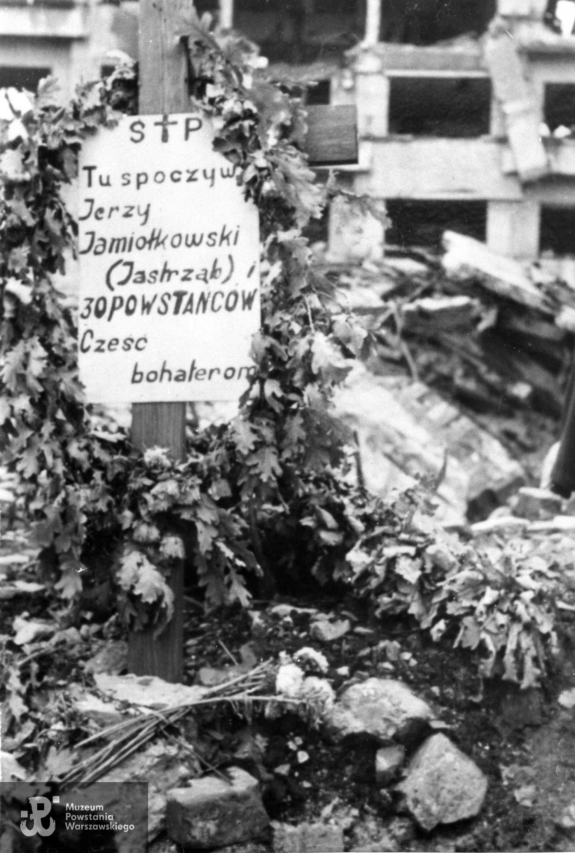 Fotografia autorstwa Zbigniewa Grochowskiego. Warszawa, 1945. Plac Trzech Krzyży. Miejsce zasypania kpr. Jerzego Jamiołkowskiego "Jastrzębia" i 30 innych Powstańców. W tle ruiny domu przy ulicy Wiejskiej róg Prusa Fot. ze zbiorów Muzeum Powstania Warszawskiego, sygn. MPW-IP/2726 (MPW-GI-4000/15/06)