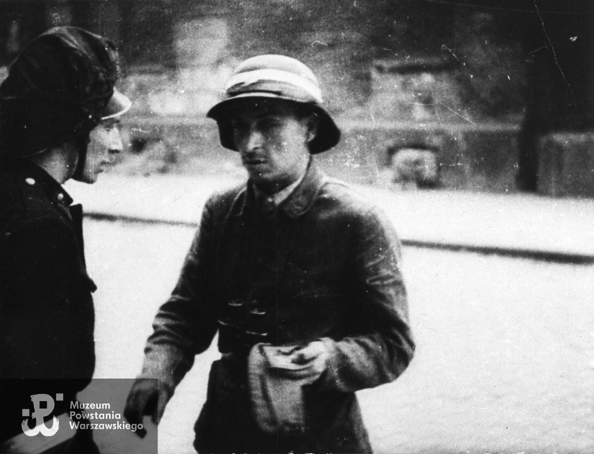 Powstanie Warszawskie, około 15.08.1944 r. Fotografia filmowa z powstańczej kroniki. Śródmieście Północne. Kpt. Wacław Zagórski "Lech Grzybowski" - dowódca II batalionu w Zgr. "Chrobry II" pomiędzy ul. Ciepłą a Placem Grzybowskim z korespondentem BIP KG AK. Na głowie kpt. Zagórskiego charakterystyczny hełm niemieckiej ochrony przeciwlotniczej. Fot. ze zbiorów Muzeum Powstania Warszawskiego, sygn. MPW-IK/1926