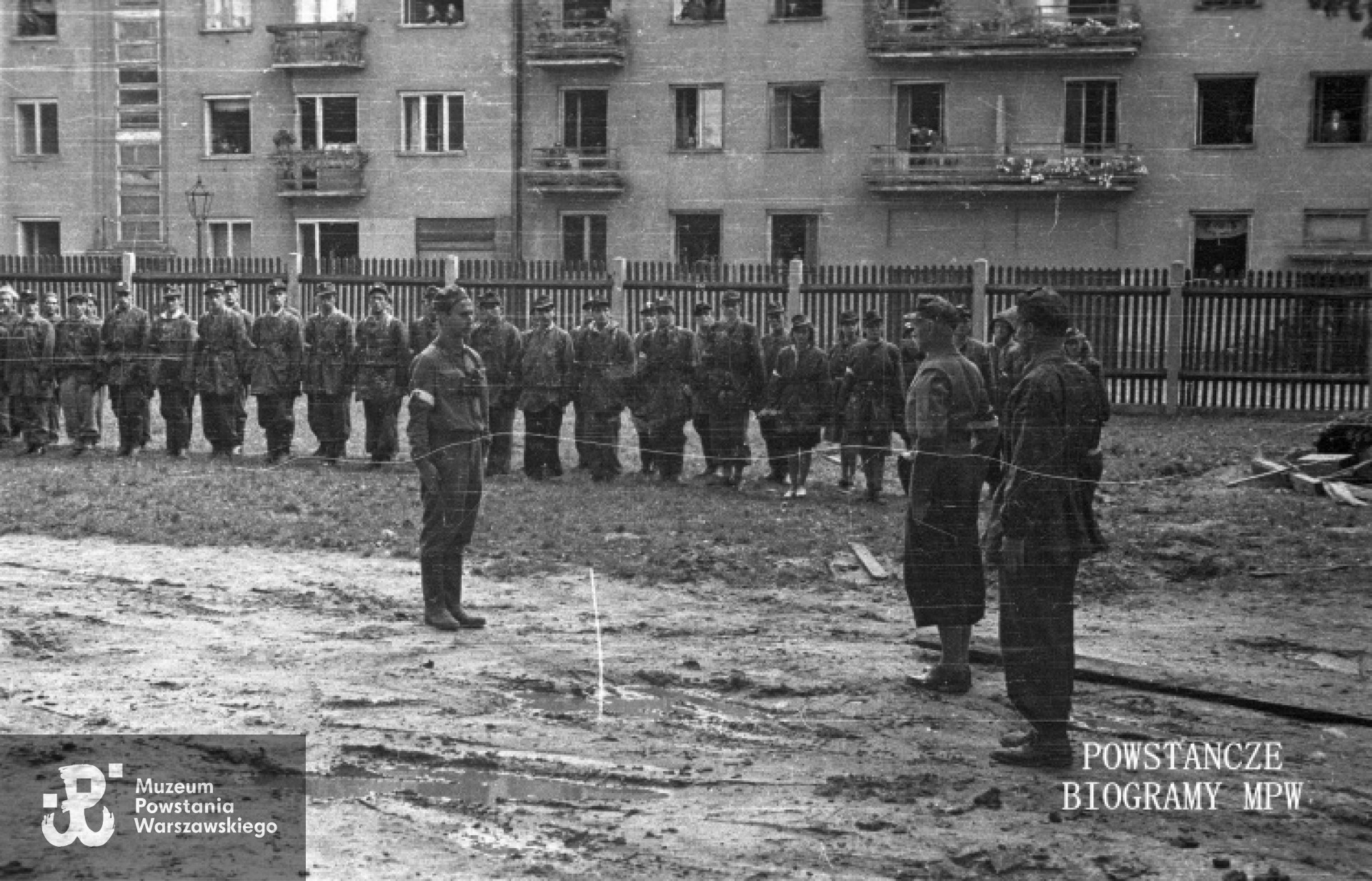 Fotografia z Powstania Warszawskiego autorstwa por.  Stefana Bałuka „Kubuś” „Starba” . Wola, 2 sierpnia 1944 Zbiórka kompanii „Zemsta” batalionu „Pięść” na terenie ogrodu Domu Starców przy ul. Karolkowej 77. Por. Stefan Matuszczyk „Porawa” składa meldunek dowódcy batalionu mjr. Alfonsowi Kotowskiemu „Okoniowi”. W tle widoczni żołnierze III plutonu i kobiecy patrol sanitarny kompanii. Za ogrodzeniem kamienice Karolkowa 82 i 84 (po lewej). Ze zbiorów Muzeum Powstania Warszawskiego, sygn. <a href="   http://www.1944.pl/galerie/fototeka/foto/7780/?szukaj=matuszczyk">MPW-IS/147</a>. Prawa autorskie : MPW
