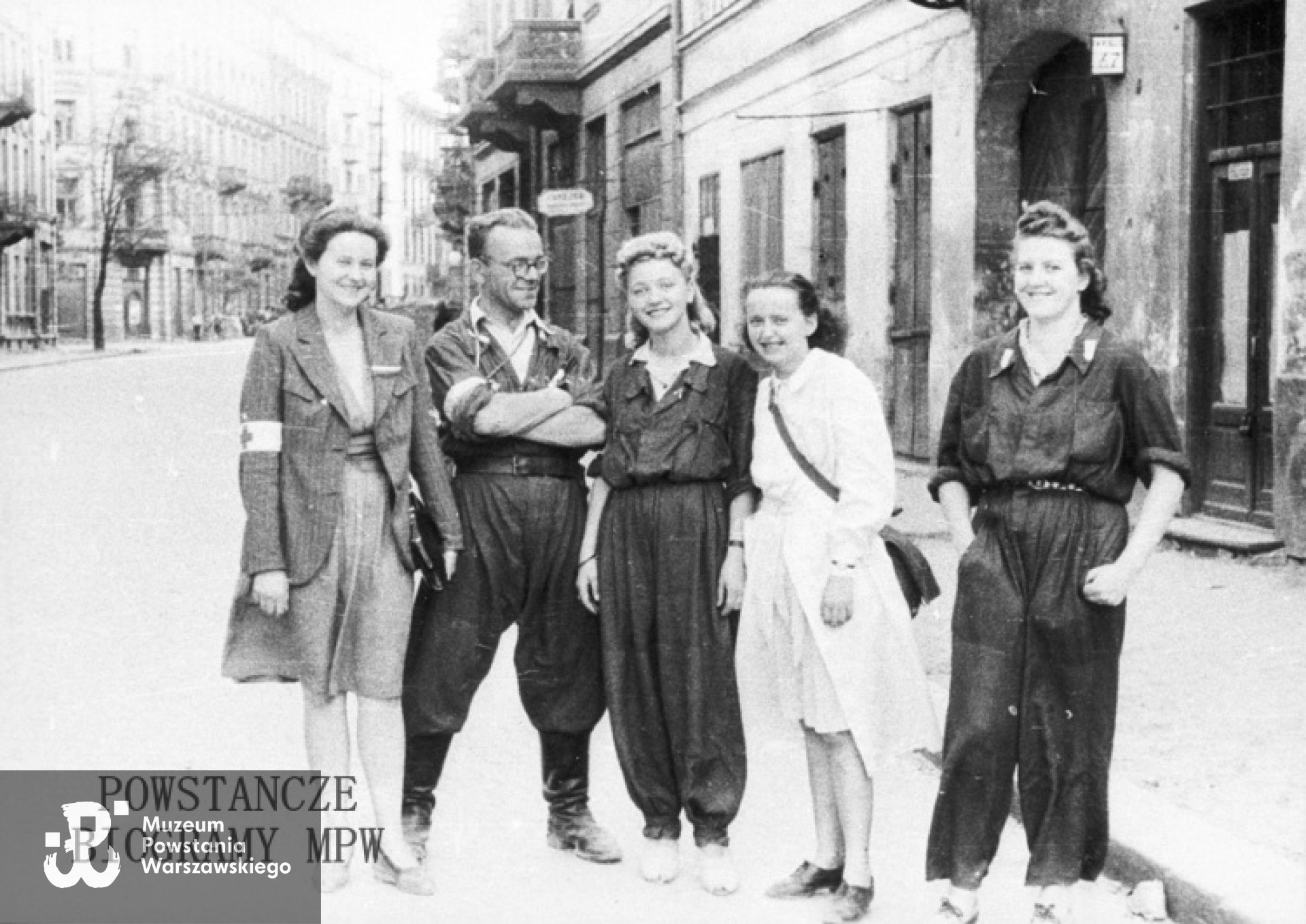 Fotografia z Powstania Warszawskiego. Śródmieście Południowe, ul. Mokotowska. Żołnierze 1. plutonu 3. kompanii "Redy" batalionu "Miłosz". Stoją od lewej: NN, ppor. Henryk Bigajski "Potocki", Daniela Białowąs-Karpińska "Nutka","Teresa", Basia Rau. Autorem zdjęcia jest Wojciech Marczyński "Bogusław". Fot. ze zbiorów Muzeum Powstania Warszawskiego, sygn.MPW-IH/5912