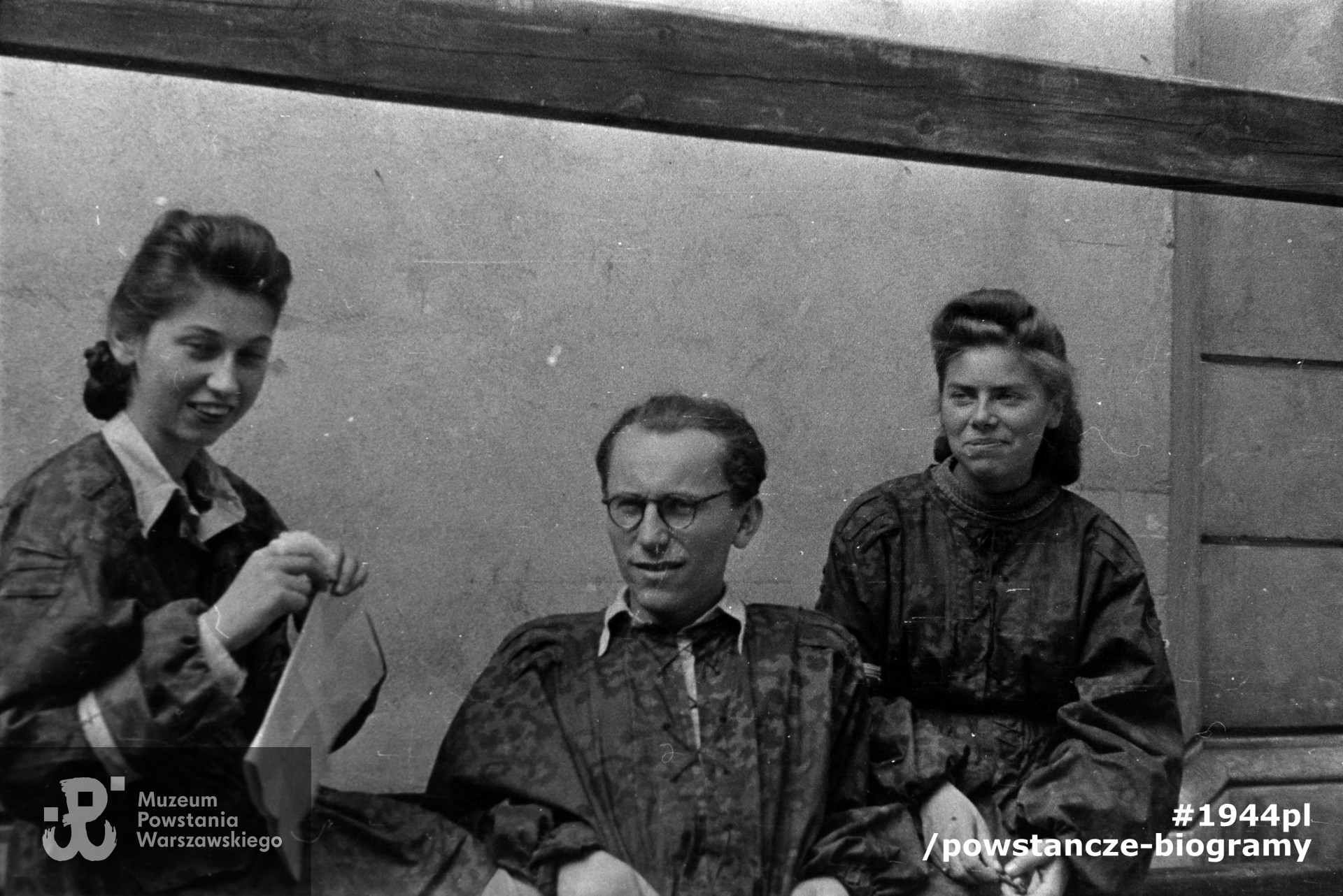  Fotografia z Powstania Warszawskiego autorstwa Dariusza Celińskiego "Aleksander": Stare Miasto, rejon ul. Długiej. Troje powstańców w panterkach, z lewej Maja Goetzen (właściwie Maria Goetzen-Pirim "Maja"),  w środku st. strz. Jerzy Bonawentura Wilhelmi "Wilk", z prawej Alicja Natansonówna (po wojnie  Skrobik). Fot. ze zbiorów Muzeum Powstania Warszawskiego, sygn. MPW-IN/11094.