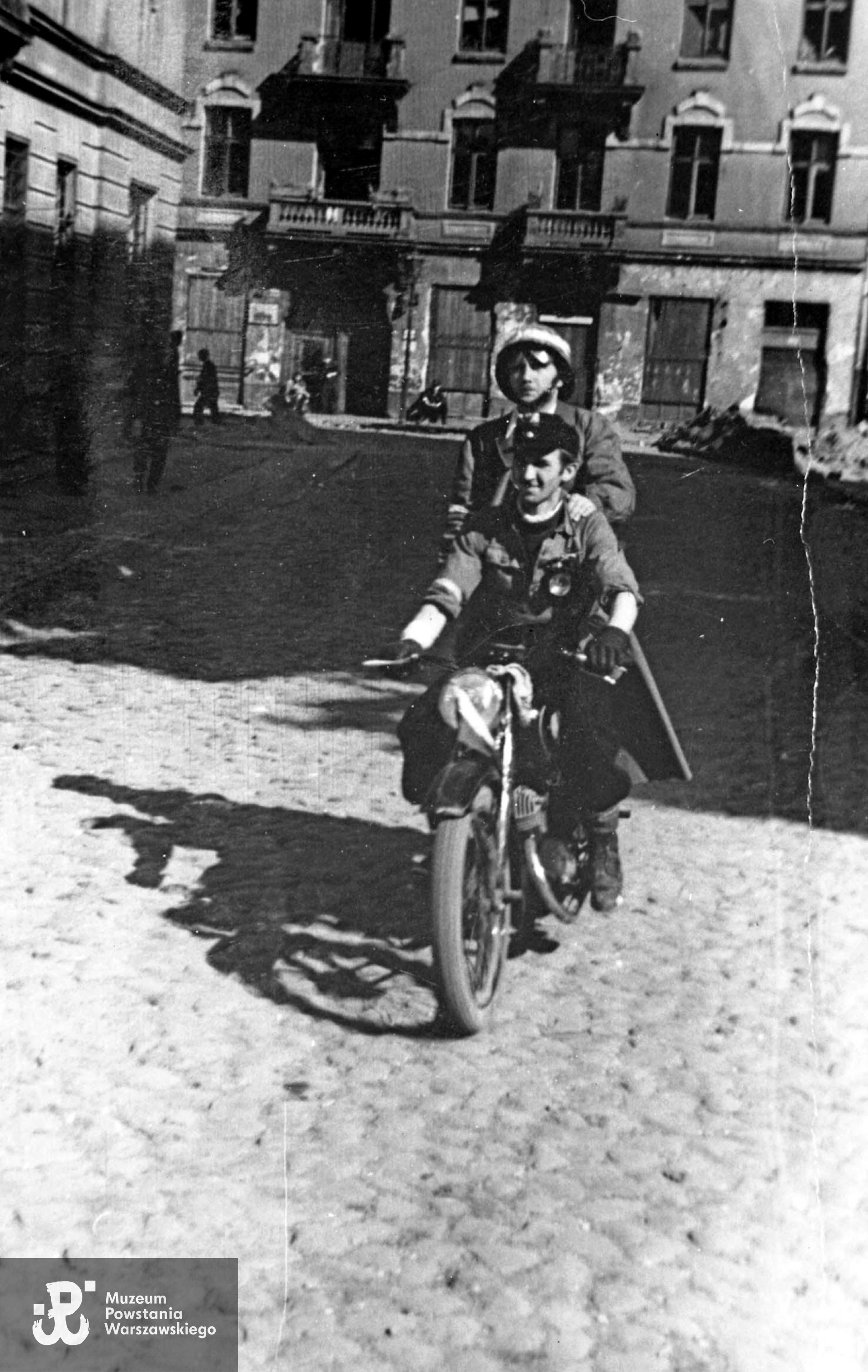 Fotografia z Powstania Warszawskiego. Śródmieście Północne. Powstańczy patrol na motocyklu na ul. Sosnowej. Ujęcie w kierunku północnym. W tle widoczna kamienica o adresie Śliska 32.  Na motocyklu siedzi prawdopodobnie plut. pchor. Kazimierz Szczeszek "Adam" (umundurowanie z wyjątkiem pilotki identyczne jak na ujęciach  MPW-IH/47 i MPW-IH/910). Fot. ze zbiorów Muzeum Powstania Warszawskiego, sygn. MPW-IH/912. Autorem zdjęcia jest Jan Żułma ps. Felix.  