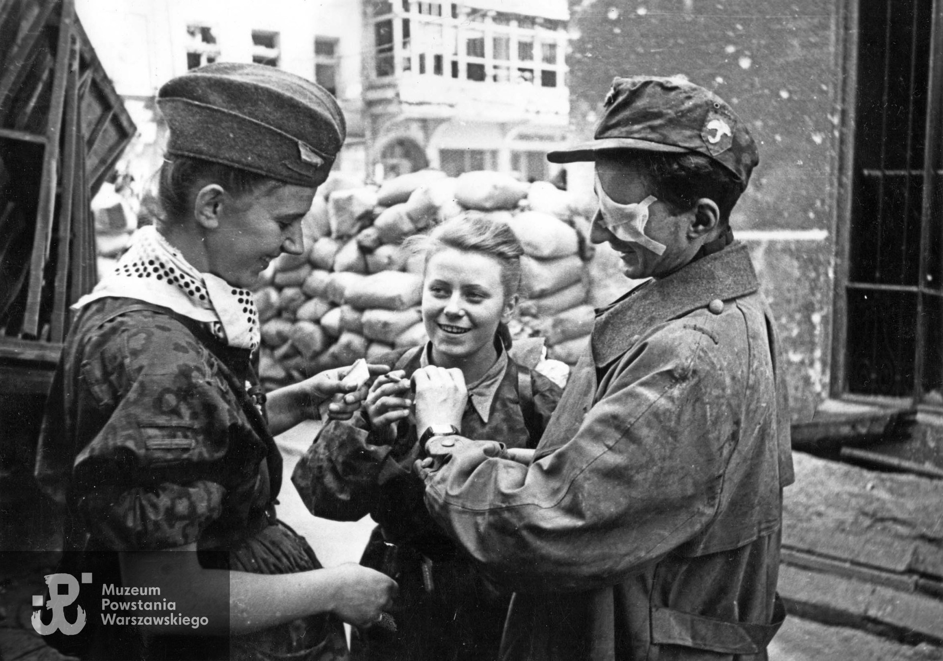 "Parasolarze" po wyjściu z kanału na ul. Wareckiej 1.09.1944 r. Zwracają uwagę: znak baonu naszyty na niemiecką czapkę polową i apaszka dziewczyny. Różnokolorowe chustki przewiązane pod szyją, w czasie walk na Starym Mieście stały się znakiem rozpoznawczym oddziałów, jednolicie ubranych w zdobyczne "panterki". Każdy oddział używał chust w innym kolorze. Od lewej stoją: nierozpoznana łączniczka lub sanitariuszka, w środku "Kama" (Maria Stypułkowska-Chojecka), po prawej ranny kpr. pchor. "Krzych" (Krzysztof Palester - poległ 21.09.1944 na Górnym Czerniakowie). W tle widoczny Hotel "Savoy" ul. Nowy Świat 58. Fot. Joachim Joachimczyk. Ze zbiorów Muzeum Powstania Warszawskiego, sygn. MPW-IK/2960.