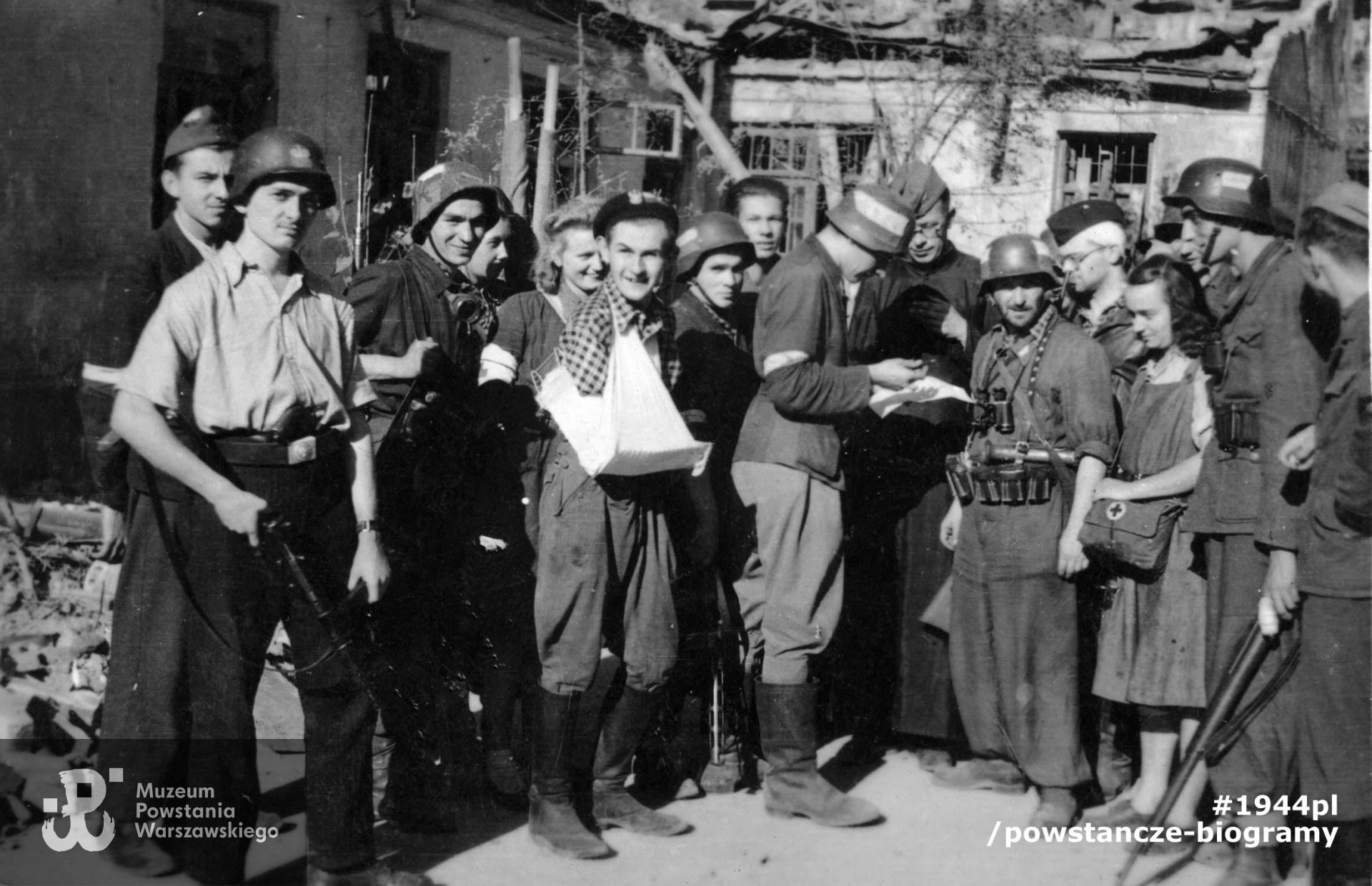 Fotografia z Powstania Warszawskiego. Śródmieście Południowe. Grupa żołnierzy 138 plutonu 1 kompanii Batalionu "Ruczaj". W środku, piąty od prawej (patrzy prosto w obiektyw) stoi plutonowy Marian Bartoszek "Kauczuk". Fot. ze zbiorów Muzeum Powstania Warszawskiego, sygn. MPW-IP/2002