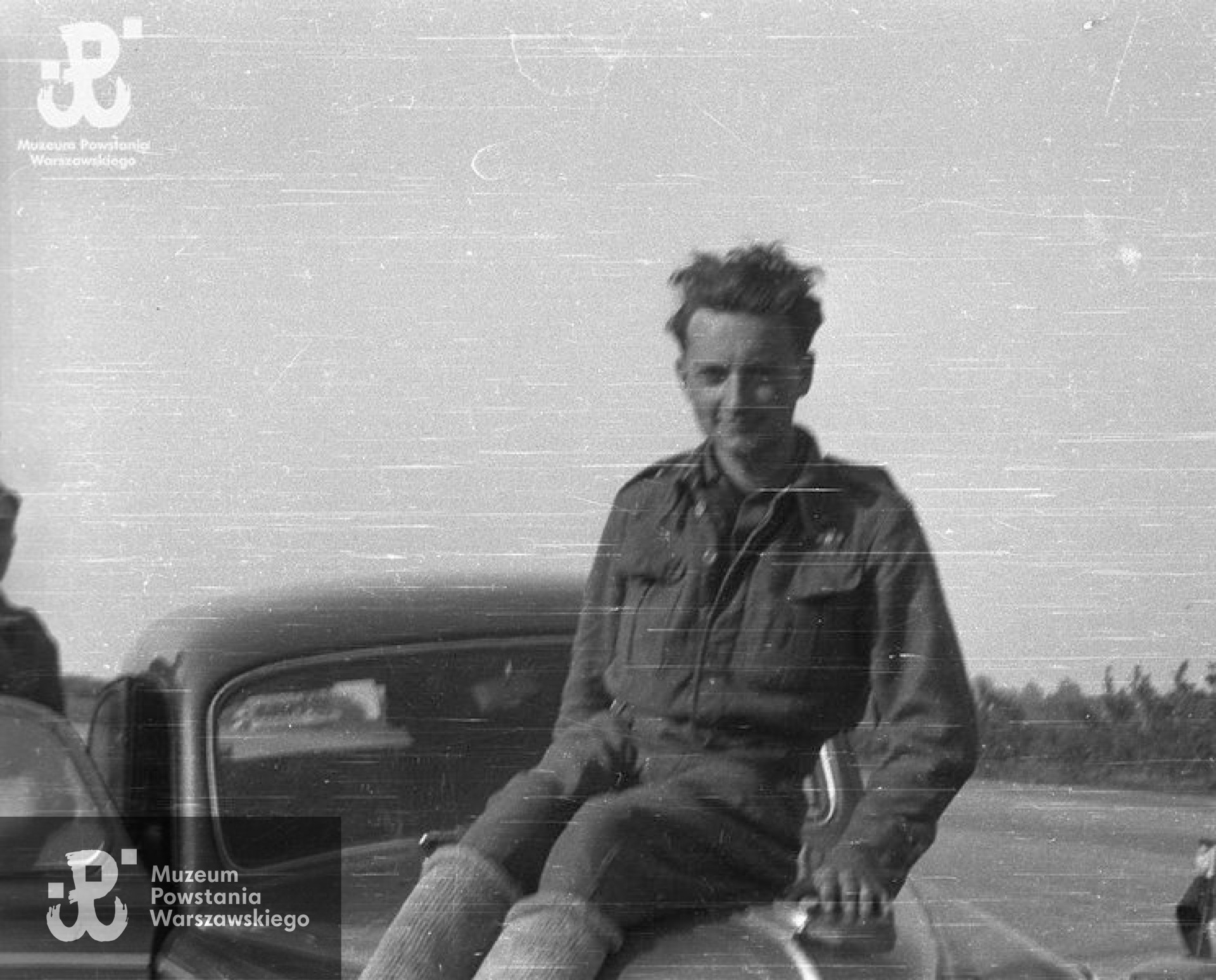 Fotografia z Oflagu X C w Lubece- maj 1945 r.  Ppor. Stefan Mączyński „Szczepcio” z kompanii harcerskiej Batalionu „Gustaw” siedzący na masce samochodu. Fot. Wiesław Chrzanowski „Wiesław”, ze zbiorów Fototeki MPW, sygn. <a href=" http://www.1944.pl/galerie/fototeka/foto/3302"> MPW-IN/3440</a>