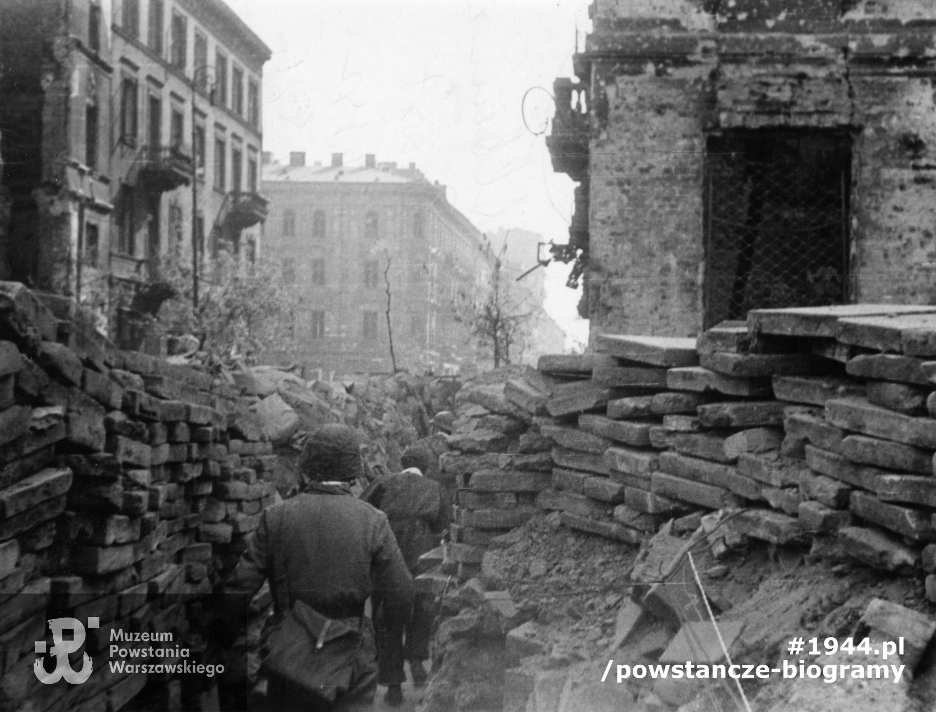 Fotografia z Powstania Warszawskiego. Śródmieście Południowe. Powstańcy z kompanii "Anna" Bat. "Gustaw" przechodzący okopem Al. Jerozolimskie na wysokości ul. Kruczej. Ujęcie w kierunku południowym. Na pierwszym planie, zwrócony tyłem, por. Wojciech Sarnecki "Wojtek". Po prawej fragment budynku Al. Jerozolimskie 15 / Krucza 49, po lewej zniszczony dom Krucza 48, następnie Krucza 46, narożna kamienica Krucza 42 / Nowogrodzka 13 i dalsze. Daleko w tle widoczna wysoka kamienica Krucza 34. Autorem zdjęcia jest Wiesław Chrzanowski. Ze zbiorów Muzeum Powstania Warszawskiego, sygn.  MPW-IK/2463