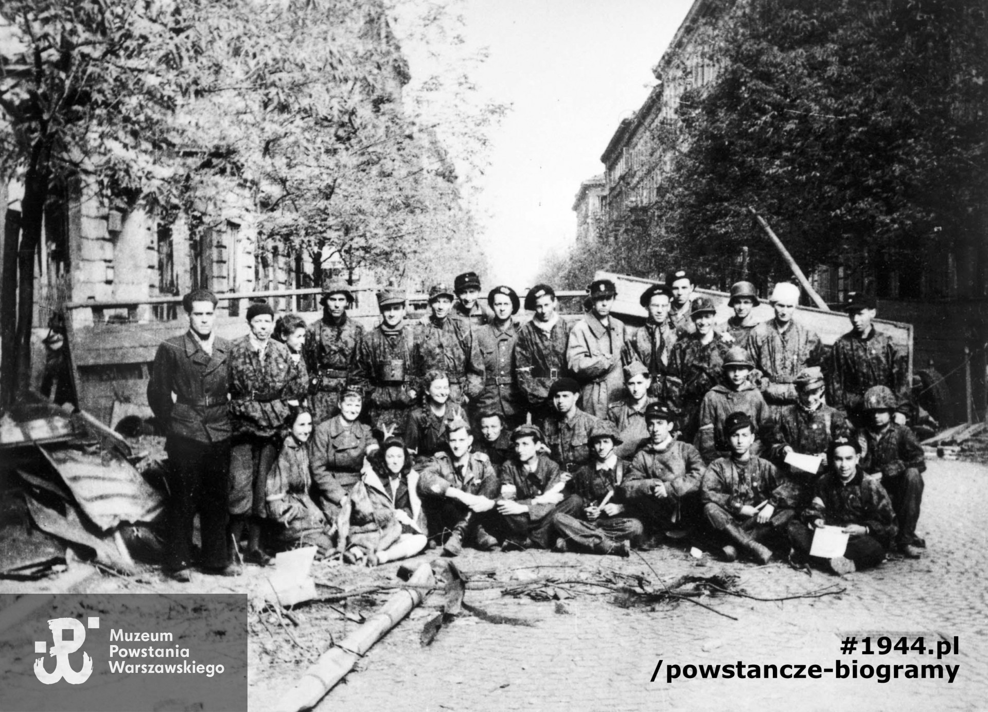 Fotografia z powstania warszawskiego. Śródmieście Południowe, ulica Krucza. Powstańcy Kompanii Harcerskiej batalionu "Gustaw". Stoją od lewej: sierż. Jerzy Mokrzyński "Broniarz" podoficer broni, hm. ppor. Witold Sawicki "Andrzej" Naczelnik HP, Małgorzata Goetzen "Rita" sanitariuszka, ppor. Janusz Gładych "Bemol" dowódca II plutonu, plut. pchor. Leszek Pecho "Ogrodziński", kpr. Janusz Żuchowicz "Grey", strz. Stanisław Bakierowski "Bat", strz. Henryk Ciok "Żbik", st. strz. Henryk Bińka "Cichy", strz. Ryszard Ksawery Ludwig "Madziar", plut. pchor. Ludwik Wojciech Wyporek "Miętus", phm. plut. pchor. Maciej Nasierowski "Brzoza", strz. Janusz Winnicki "Sas", kpr. pchor. Waldemar Kaczorowski "Jurkowski", hm. sierż. pchor. Kazimierz Burmajster "Zenon" "Burek", strz. Bogusław Godebski "Jabłoński" łącznik, sanitariuszka Anna Szatkowska "Anna", sanitariuszka Ewa Marszałek "Iza", sanitariuszka Barbara Miszewska "Lidka", phm. Anna Sadkowska "Sosnowska" sanitariuszka, hm. ppor. Tadeusz Iłłakowicz-Naczko "Krakowski", "Dada" dowódca plutonu III, sanitariuszka Aleksandra Jabłońska "Maria", "Babcia", phm. Marek Jarosz "Ciszkowski" łącznik, ppor. Jerzy Łopuszański "Korwin" instruktor wojskowy i zastępca dowódcy kompanii, phm. Lucjan Krause "Leonidas" łącznik, hm. ppor. Zbigniew Fallenbuchl "Wilanowski" dowódca I plutonu, strz. Stanisław Lubowiecki "Staszek", kpr. z cez. Bogusław Frąckiewicz "Bob", łącznik Janusz Kuć "Świt", łącznik Jerzy Zawieska "Senacki", łącznik Sławomir Piasecki "Sokół", łącznik Jerzy Świderski "Lubicz". Fot. ze zbiorów Muzeum Powstania Warszawskiego, sygn. MPW-IH/166