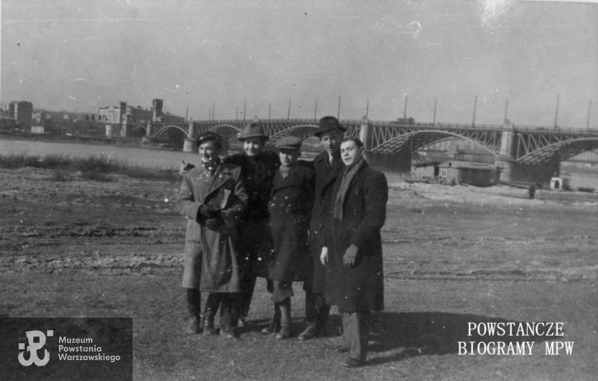 Fotografia z okresu okupacji niemieckiej. Grupa młodych mężczyzn na praskim brzegu Wisły. W tle most Poniatowskiego. Od lewej: Aleksander Kamiński, Tadeusz Blejarski, Stefan Bilski, Leszek Szymańczyk, Zadrożny. MPW-IP/5253