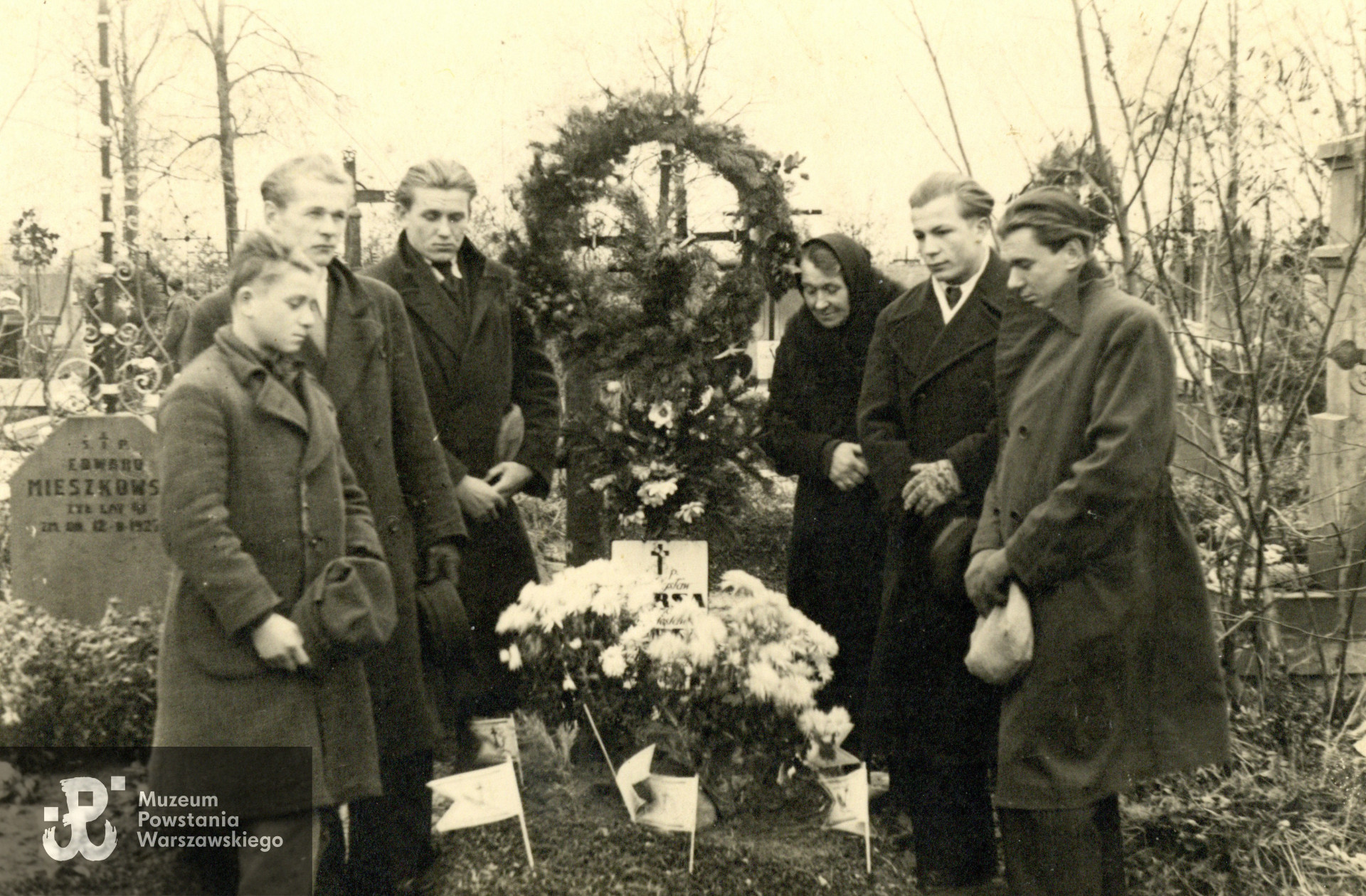 Fotografia powojenna, prawdopodobnie 1945 r., Cmentarz Bródnowski w Warszawie, miejsce pochowania Władysława Pursy (1894-1944) i jego syna Jana (1928-1944), pierwsza mogiła z metalowym krzyżem. Przy grobie stoją:  najbliżej krzyża żona - Marianna Pursa (II-voto Borusiewicz) oraz  syn Adolf Pursa ps. Grajdołek (pierwszy od prawej). Fotografia ze zbiorów rodzinnych, udostępniona przez wnuczkę p. Elżbietę Wysocką