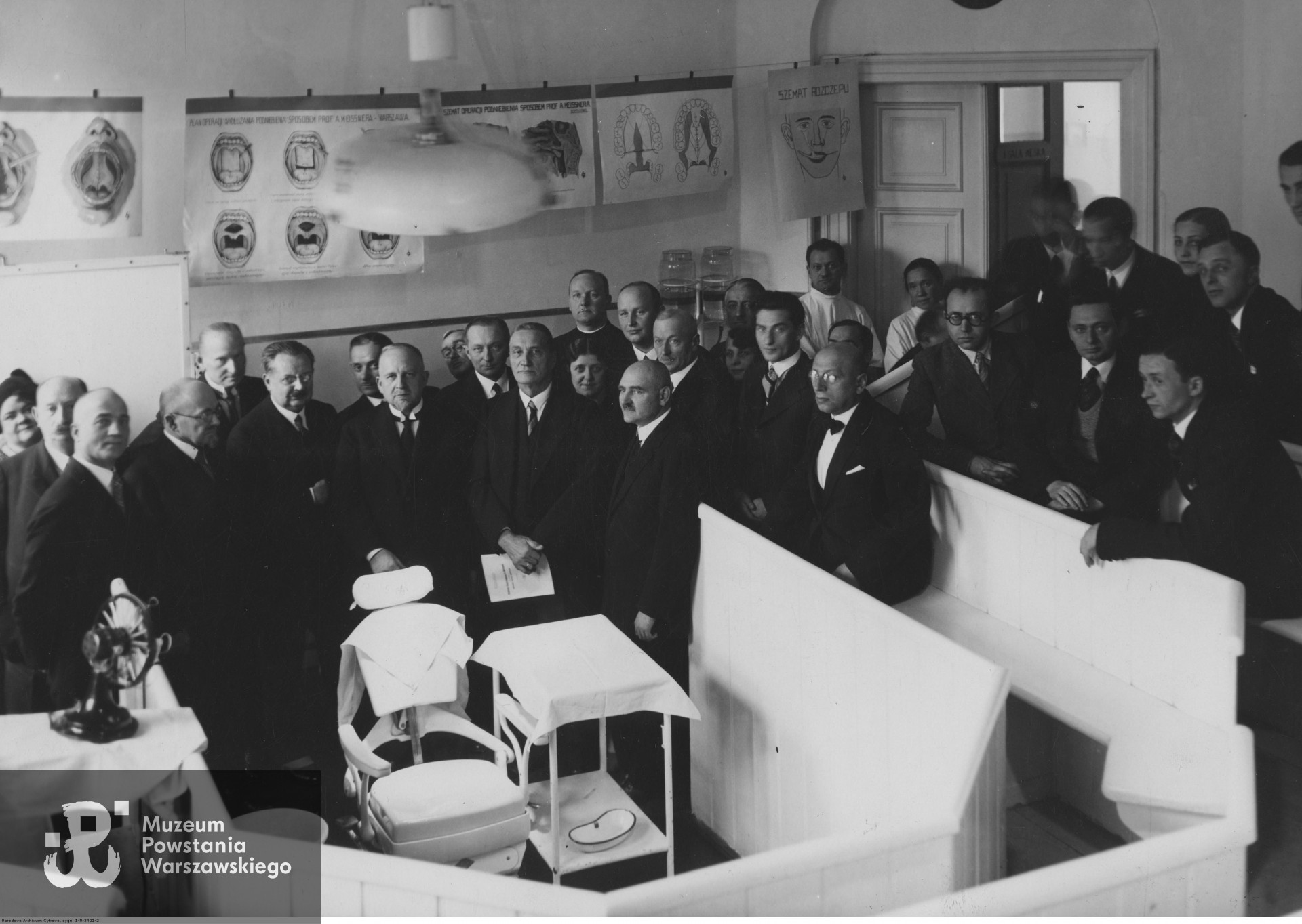 Zwiedzanie sali wykładowej w jednej z nowo otwartych klinik w Akademii Stomatologicznej w Warszawie. W pierwszym rzędzie stoją od lewej: profesor Akademii Stomatologicznej w Warszawie Alfred Meissner, rektor Akademii Stomatologicznej w Warszawie profesor Roman Nitsch, profesor Uniwersytetu Lwowskiego doktor Aleksander Cieszyński, dyrektor Departamentu Szkolnictwa Średniego Ministerstwa Wyznań Religijnych i Oświecenia Publicznego doktor Zygmunt Zagórowski. Widoczny fotel dentystyczny; na ścianach wiszą plansze dydaktyczne. Zdjęcie ze zbiorów Narodowego Archiwum Cyfrowego sygnatura 1-N-3421-2